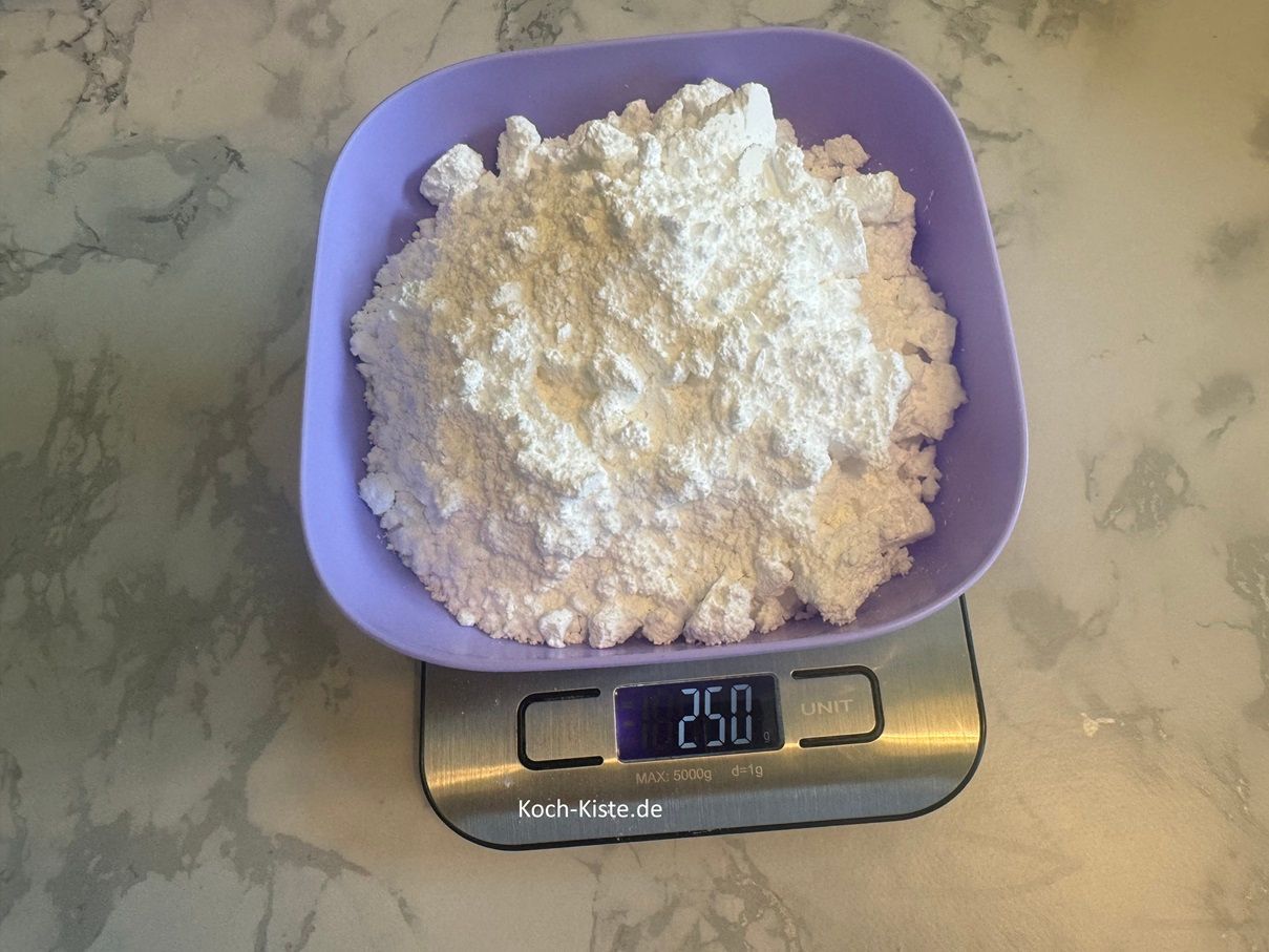 Nun musst Du einiges abwiegen. Beginne damit eine Schale auf die Küchenwaage zu stellen auf 0 und 250 g Puderzucker abzuwiegen.