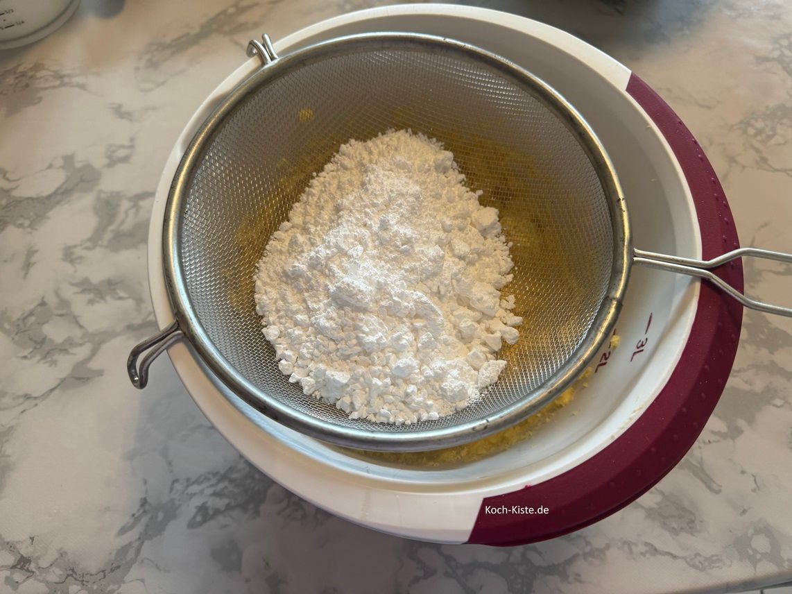 lege ein Küchensieb auf die Rührschüssel mit dem Ei-Butter Gemisch, kippe den Puderzucker in das Sieb und streiche mit der Esslöffel Rückseite den Puderzucker durch das Sieb