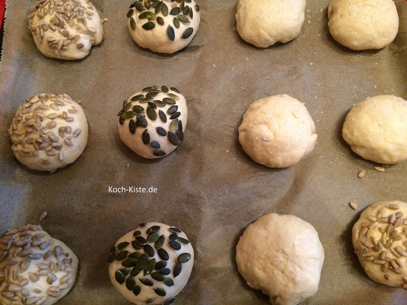 Bestreiche die Teiglinge mit Wasser und belege sie mit Körnern deiner Wahl. Drücke die Körner etwas in den Teig, damit sie beim Verzehr nicht gleich abfallen.