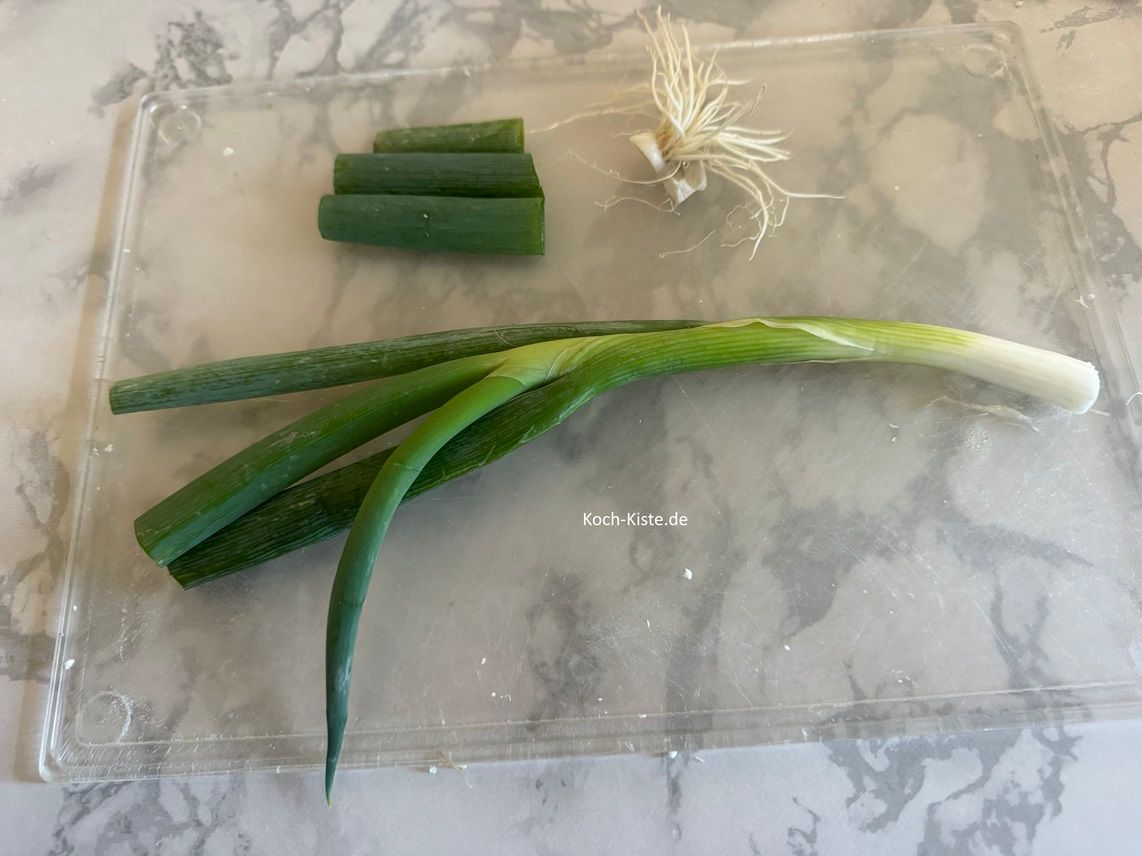 Nun sind die Lauchzwiebeln dran. Lege 1 Lauchzwiebel auf das Schneidebrett und entferne unten das Wurzelstück und oben ein bisschen von dem Grünen.