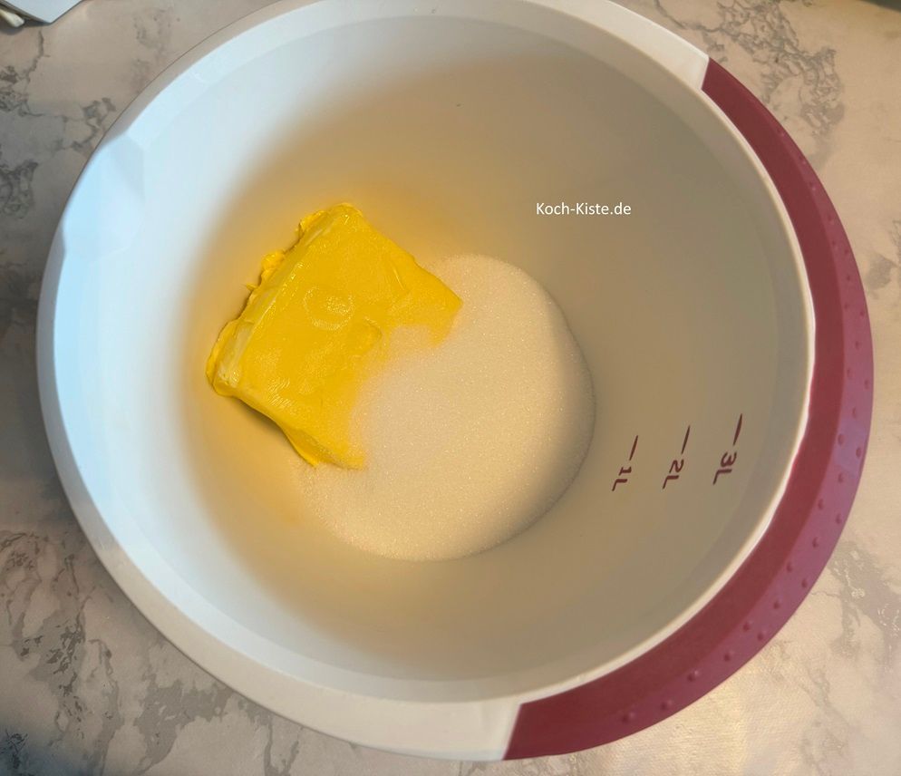 gebe das Packet weiche Butter in die Rührschüssel . Dann stelle die Rührschüssel auf die Küchenwaage auf 0 und wiege 200 g Zucker hinein