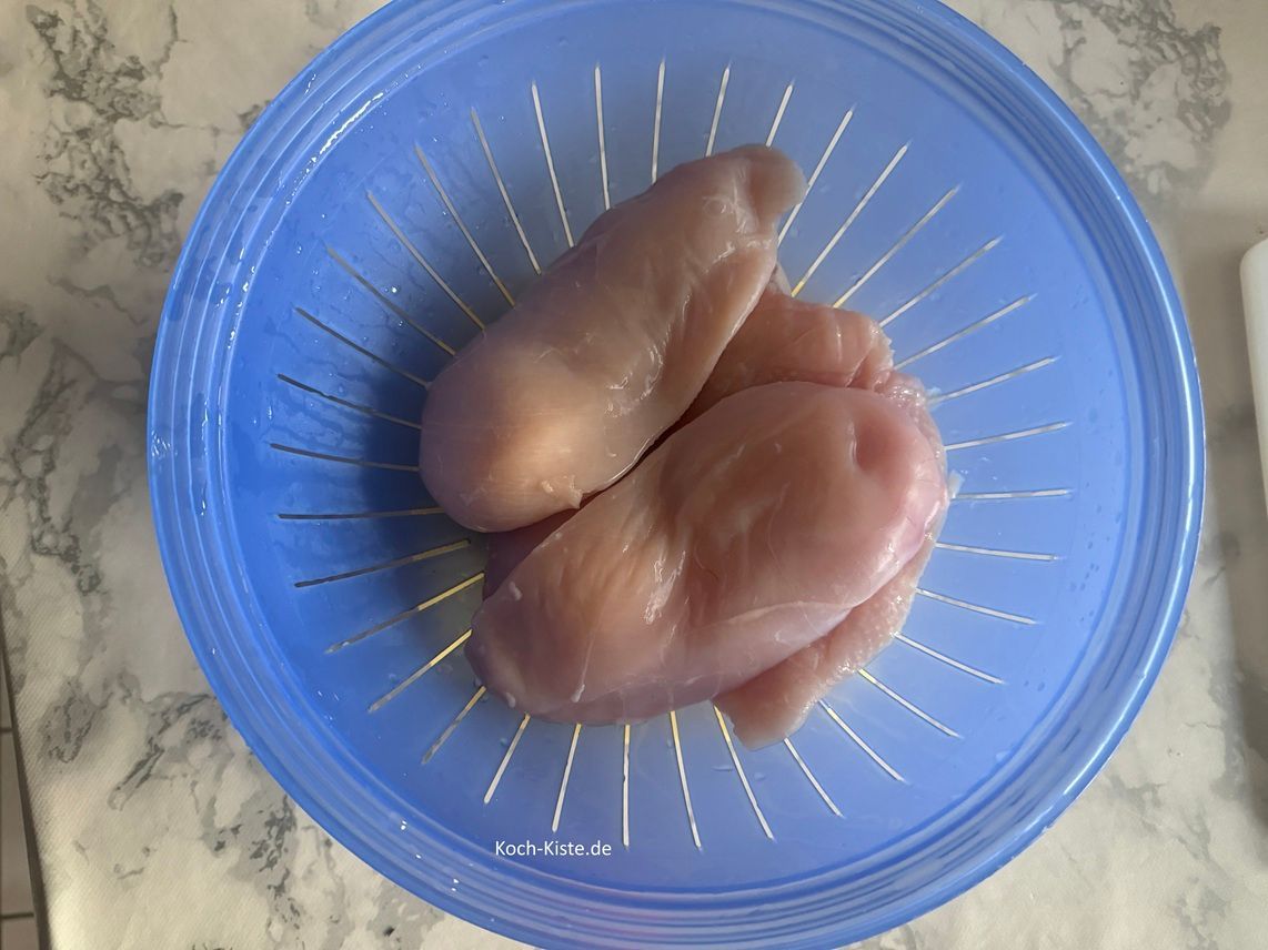 halte die Hähnchenbrustfilets nacheinander unter kaltes, fließendes Wasser und lege sie dann in ein Küchensieb. Das Küchensieb stelllst Du auf einen Teller und dann auf die Arbeitsfläche.