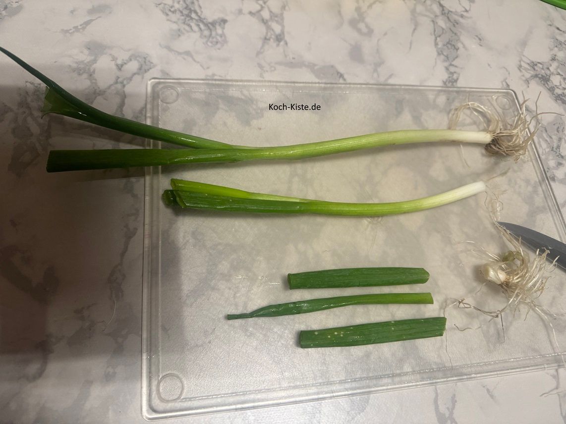 lege die Lauchzwiebel auf das Schneidebrett, entferne das Wurzelstück und etwas von dem Grünen oben