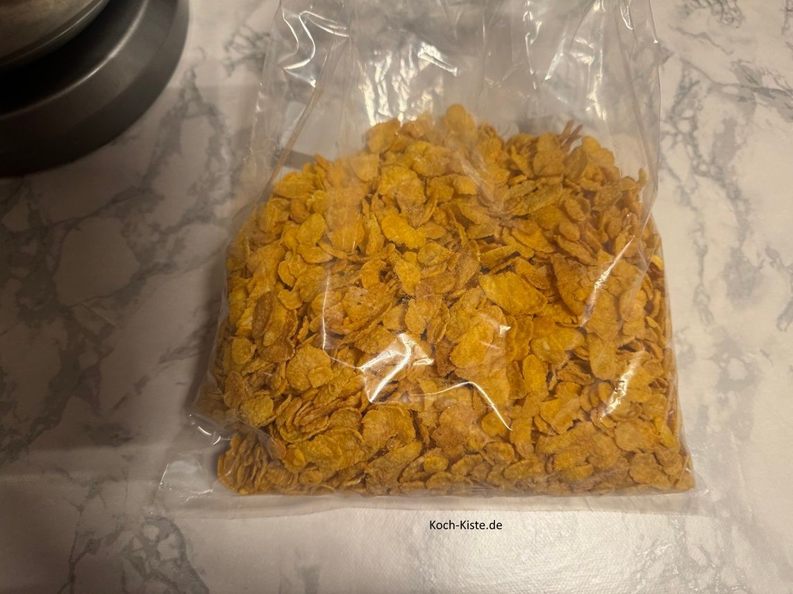 stelle eine extra Schüssel auf die Küchenwaage auf 0 und wiege 250 g Cornfläkes oder Choco Pops ab . Schütte diese in einen Gefrierbeutel