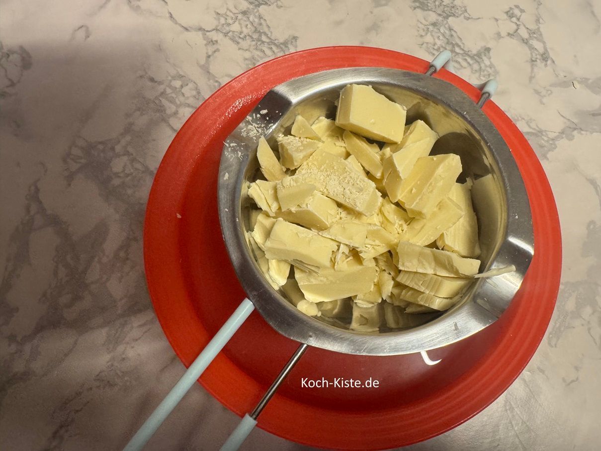 fülle die Kuvertürestücke in die Schmelzschale. Die Schmelzschale legst Du auf eine Schüssel und in die Schüssel gießt Du kochendes Wasser . Dann verrühre die Kuvertüre mit dem Teelöffel bis sie geschmolzen ist.