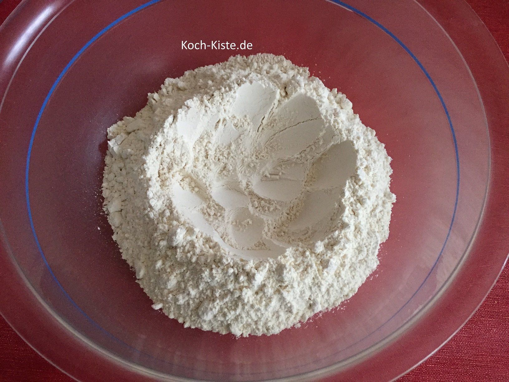 gebe das Mehl in eine große Rührschüssel und fertige mit einem Esslöffel eine Mulde an