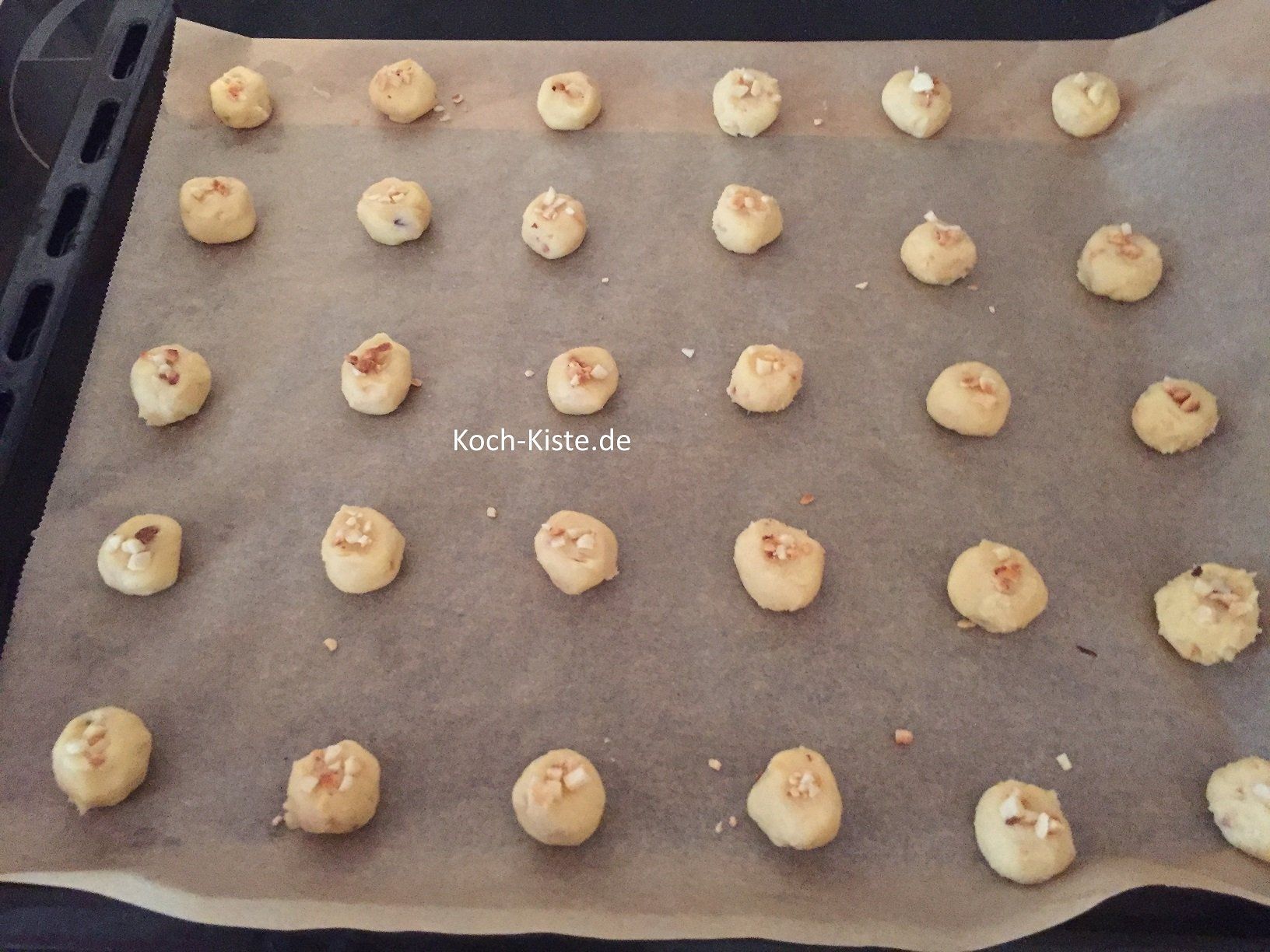 jede Teigkugeel obenauf etwas platt drücken und von der Mandeln-Nuss Mischung etwas drauf geben