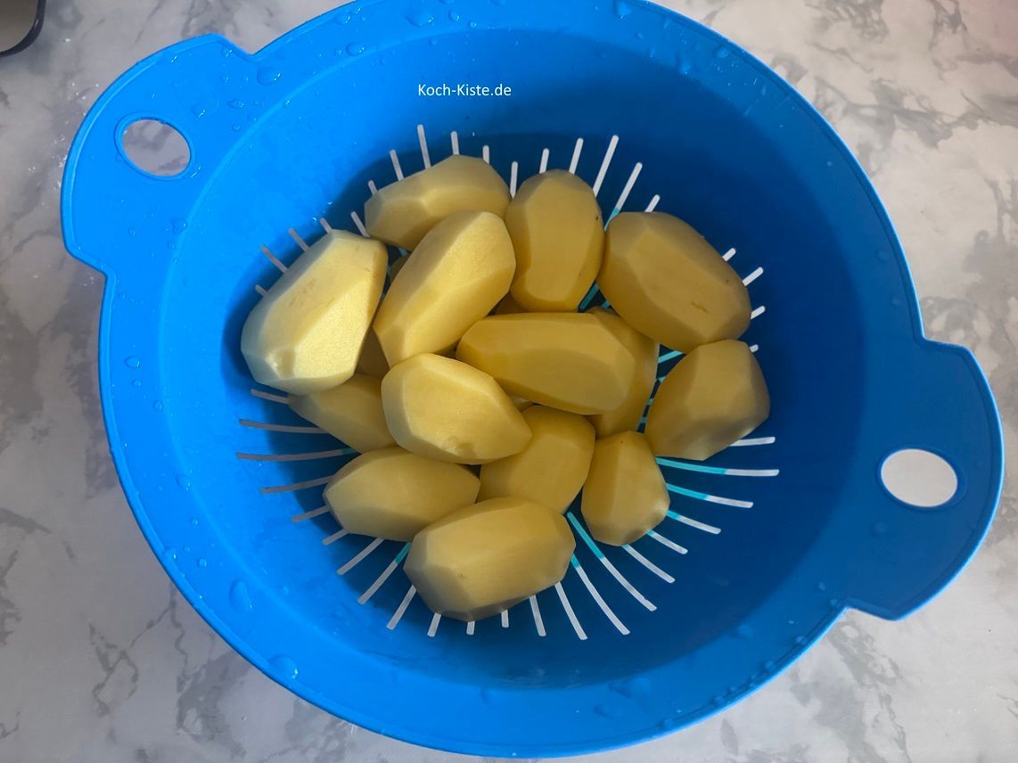 beginne damit 1,5 kg Kartoffeln zu schälen, in ein Küchensieb zu geben und unter kaltem, fließendem Wasser abzuspülen