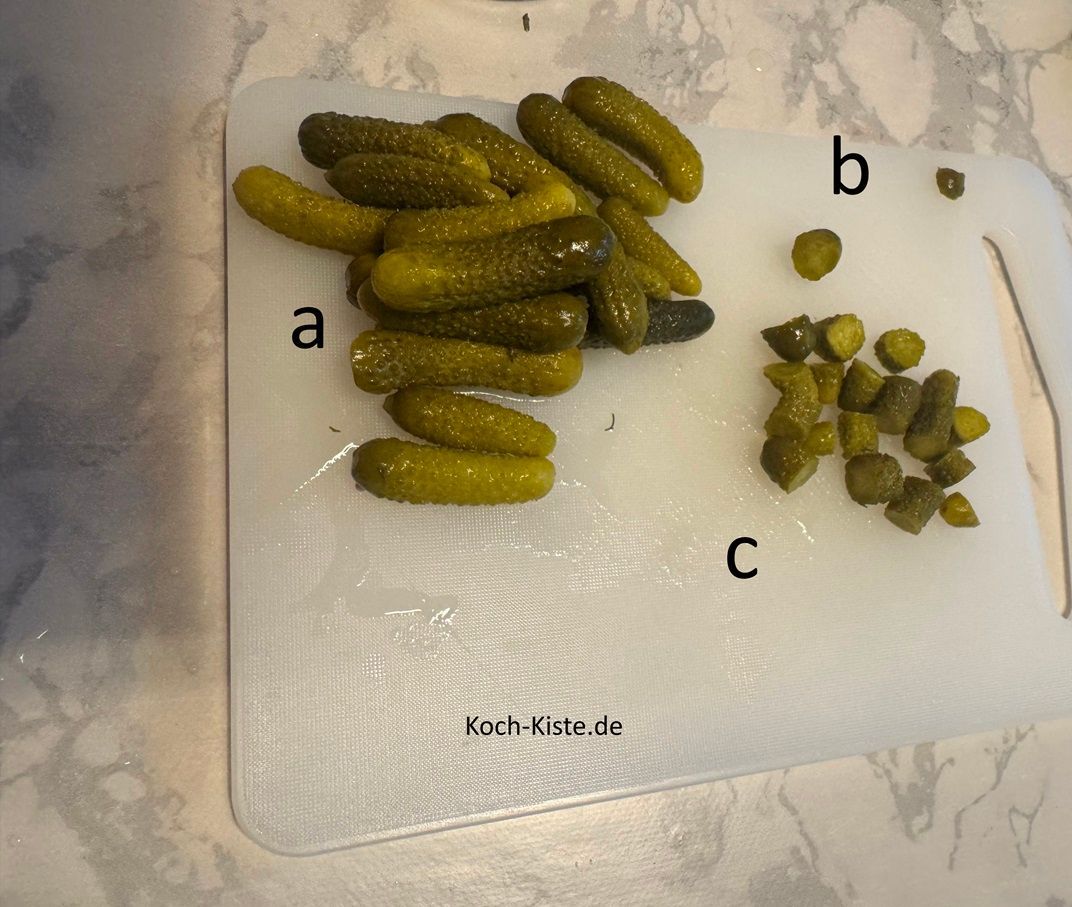 entnehme die Chornichons auf das Schneidebrett (a), etferne eventuell vorhandene Stiele (b) und schneide sie in kleine Stücke