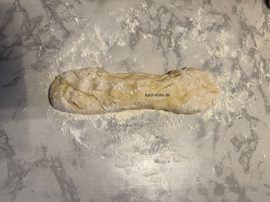 gebe etwas Dinkelmehl auf die Arbeitsfläche und ziehe dir V inyl- Einmalhandschuhe an. Gebe 1 Teigration auf die Arbeitsfläche und rolle ihn etwas zusammen