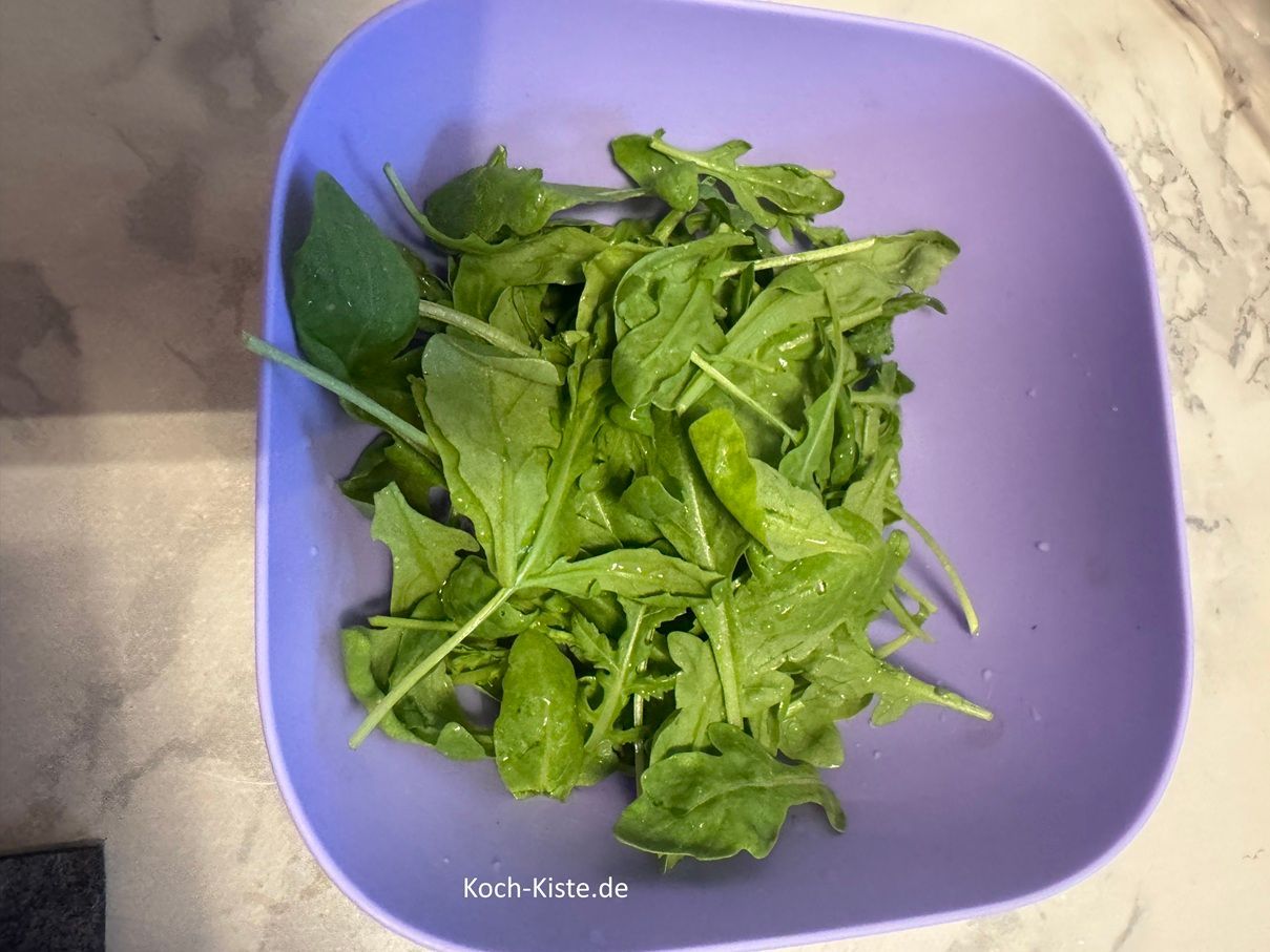 stelle wieder eine Schale auf die Küchenwaage - auf 0 und wiege 50 g Rauke ab. Dann gebe die Rauke in das kleine Küchensieb und spüle sie unter kaltem, fließendem Wasser ab. Lasse die Rauke gut abtopfen.