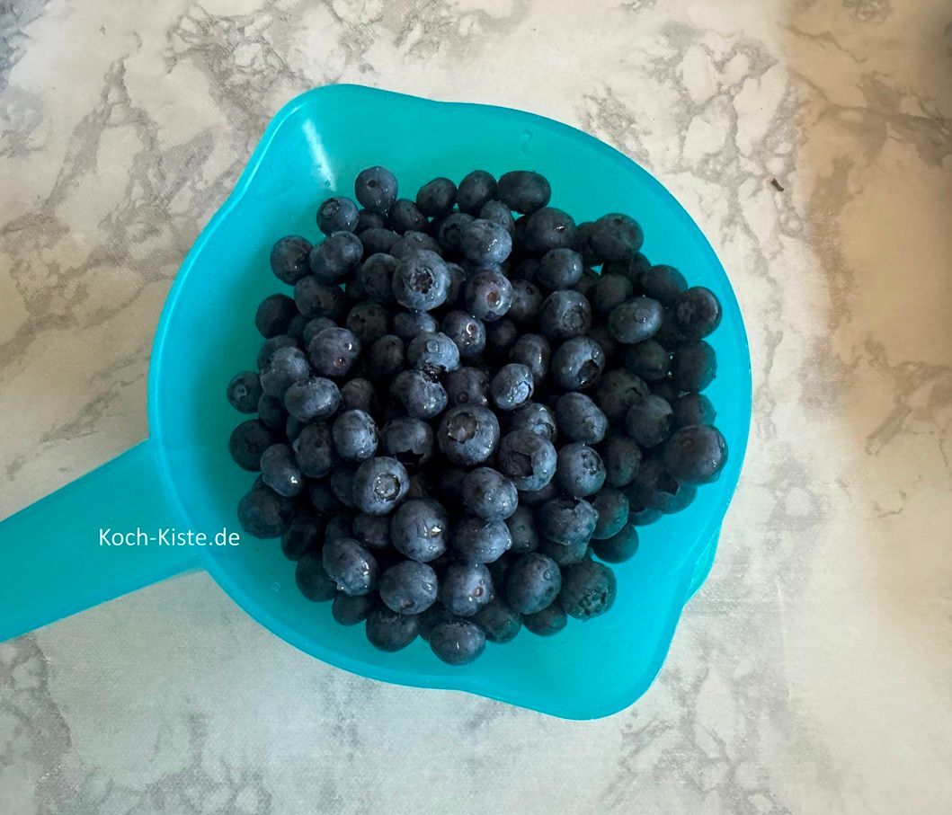 gebe die Blaubeeren in ein Küchensieb und spüle sie unter kaltem, fließendem Wasser ab. Dann stelle das Küchensieb auf einen Teller und lasse alles abtropfen.