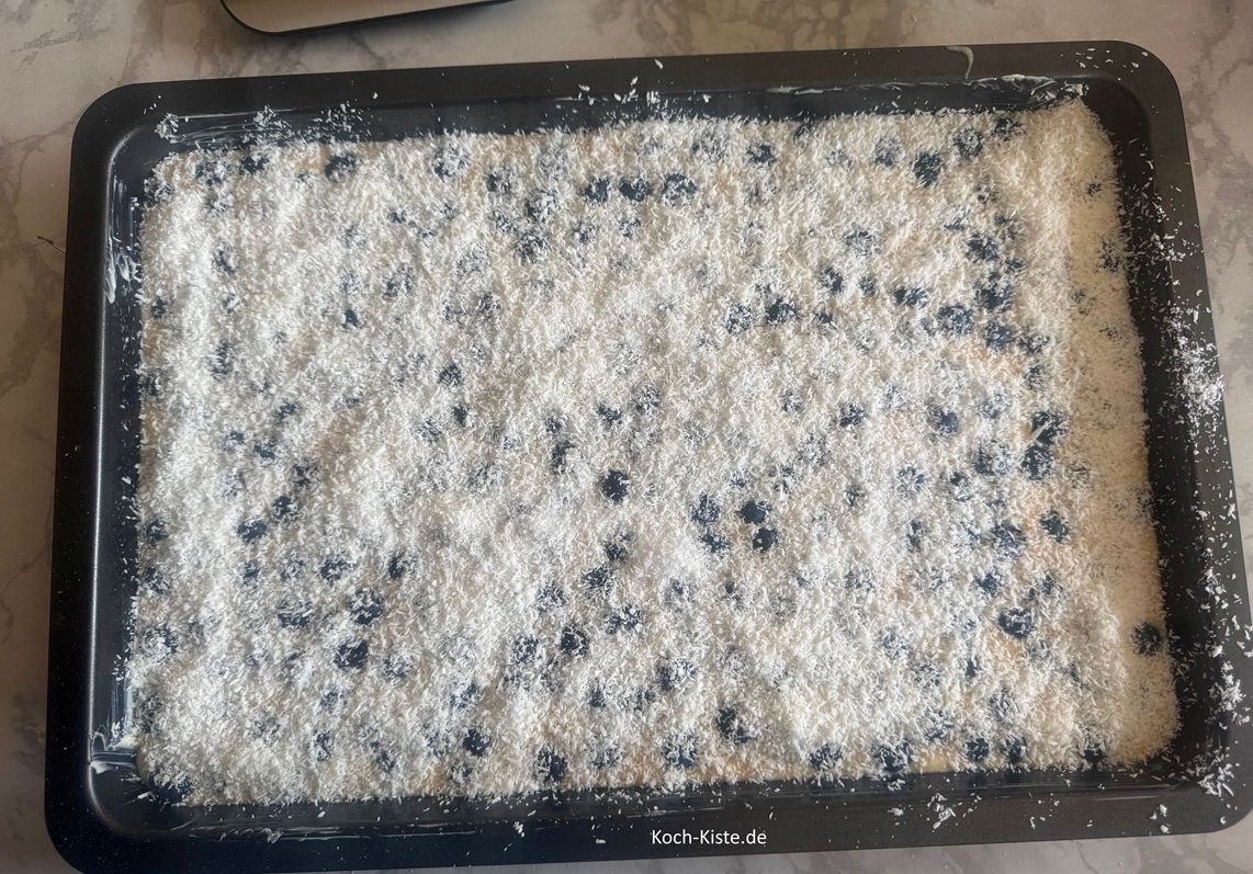 Nun verteile die Kokosmischung gleichmäßig auf dem Teig