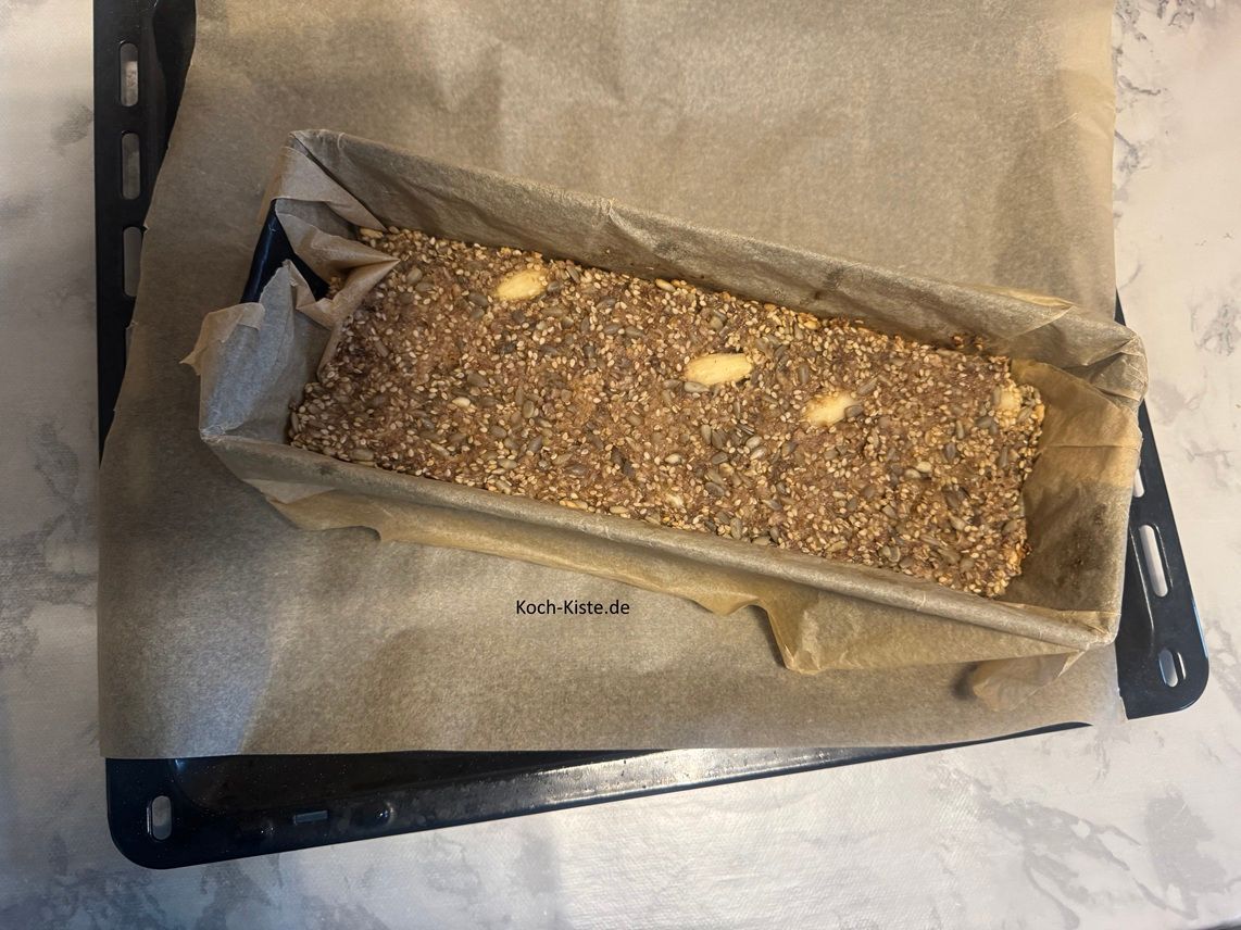 Ziehe Dir Küchenhandschuhe an, neheme die Kastenform aus dem Backofem und stelle sie auf die Untersetzer / oder das Backblech .Hebe an den Backpapierseiten das kernige Eiweißbrot aus der Kastenform