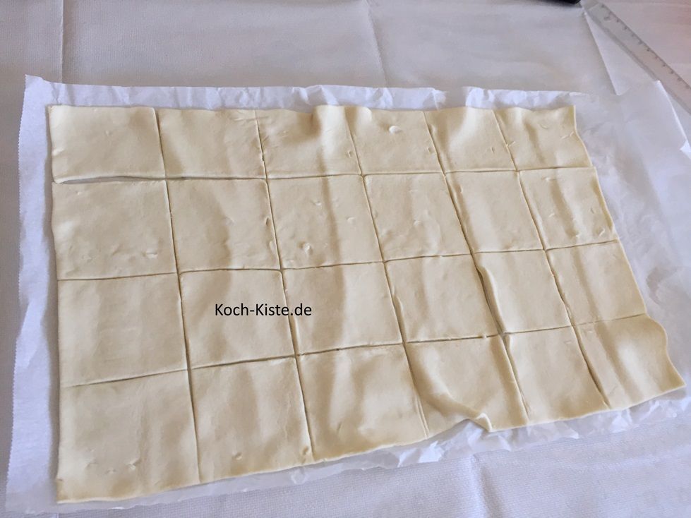 rolle den Blätterteig auseinander und teile ihn in 24 Stücke. Du kannst entweder mit einem Lineal arbeiten oder den Teig falten und leicht andrücken, so dass Du die Linie (vom Falten) erkennen kannst.
