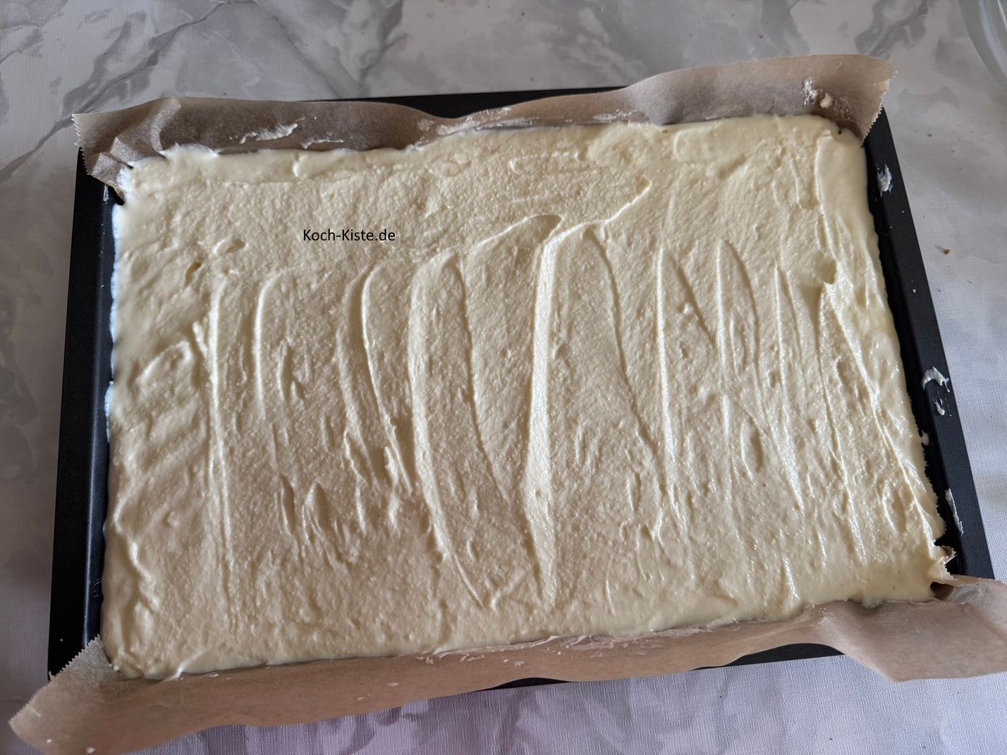 nun wird mit Hilfe des Teiglöffels die Quarkmasse oben auf gegeben , gleichmäßig verteilt und möglichst glatt gestrichen