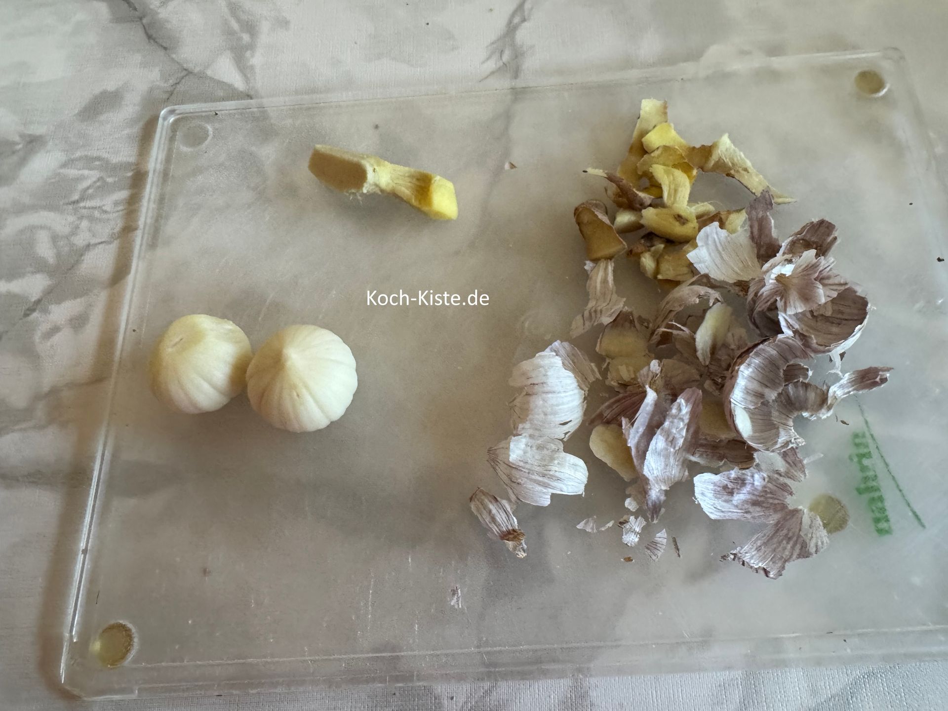 dann lege eine Knobizehe auf das Schneidebrett und schneide oben und unten eine Scheibe ab. Nun kannst Du die Knobizehe pellen. Wiederhole die Schritte bei der 2 Knobizehe. Als nächstes nehme das Gemüsemesser und schäle den Ingwer.. Es kann sein das Du ihn an einigen stellen etwas dicker schälen musst, da Ingwer manchmal trockene / holzige Stellen haben kann.