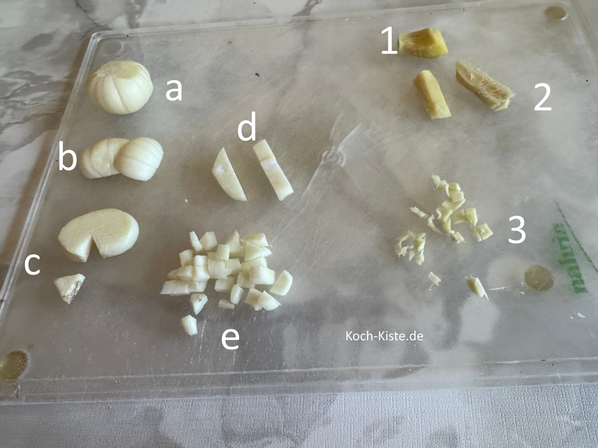 lege 1 Knobizehe auf das Schneidebrett (a), schneide sie in Scheiben (b) , dann entferne den Knoblauchkeil (c) , schneide den Knobi nun in Streifen (d) und dann in kleine Stücke (e). Wiederhole alle Schritte bei der 2 Knobizehe. Als nächstes lege den Ingwer auf das Schneideberett (1) , schneide ihn in dünne Streifen (2) und dann in kleine Stücke (3)