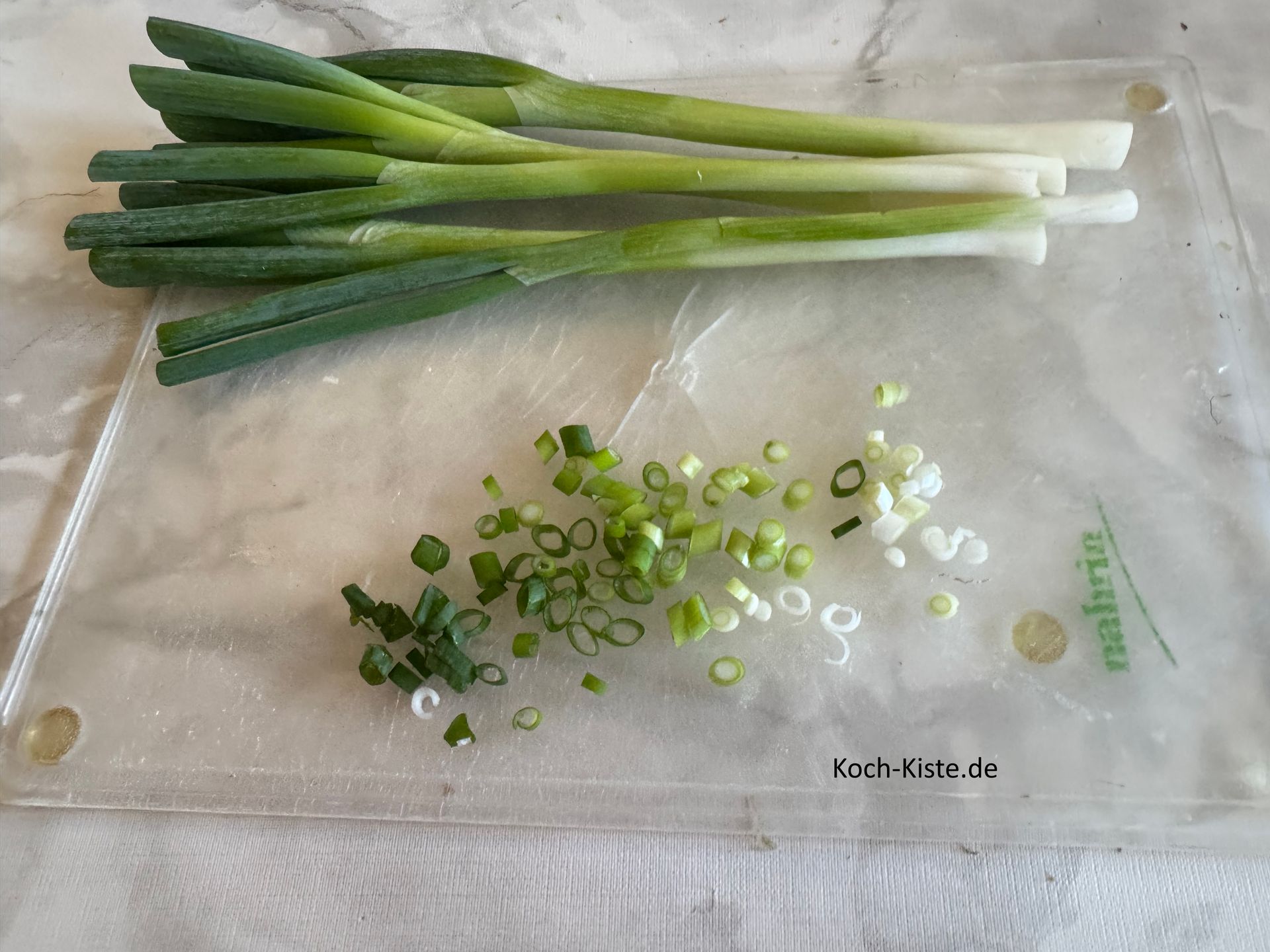 dann schneide die Frühlingszwiebel oben am Grünansatz leicht schräg ein, nun kannst Du die äußere Schicht nach unten hin abziehen. Danach wird die Frühlingszwiebel in kleine Stücke geschnitten. Wiederhole die Schritteb bei allen Frühlingszwiebeln.