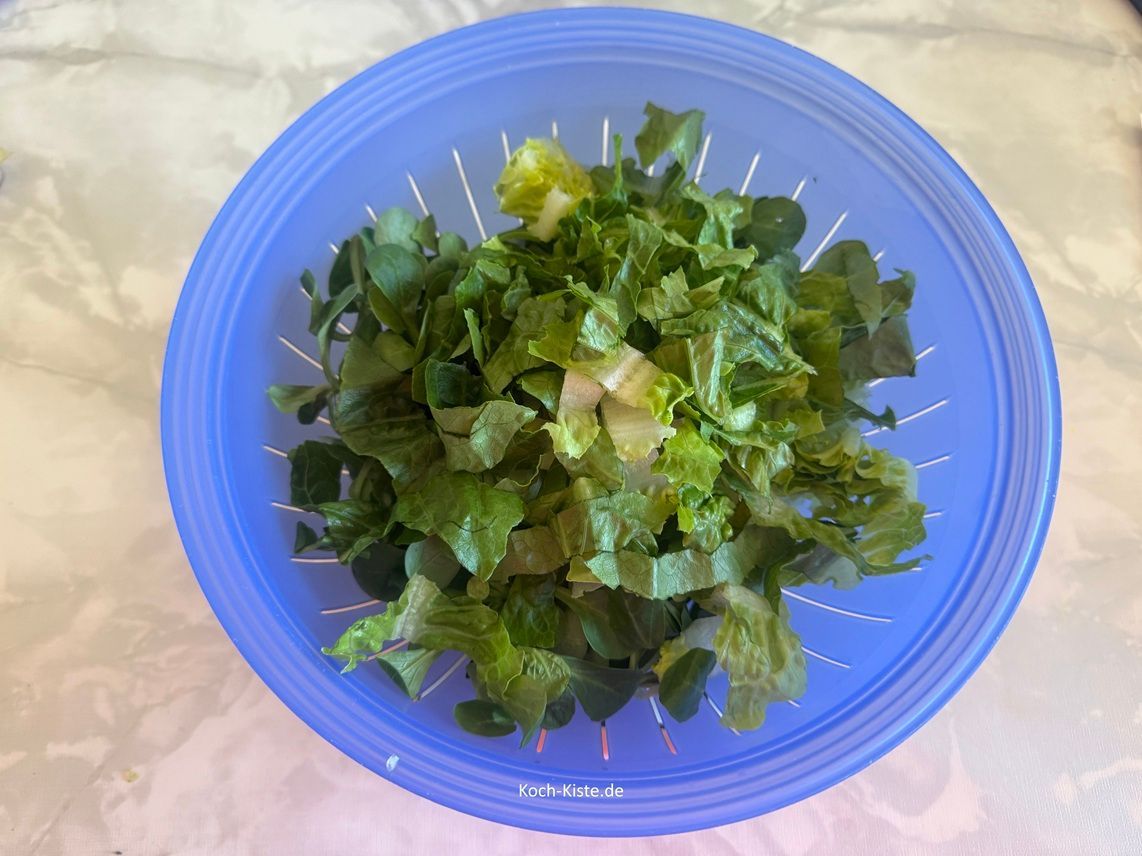 beginne damit 160 bis 200 g gemischte Salatblätter, über ein Küchensieb in mundgerechte Stücke zu schneiden. Dann spüle den Salat unter kaltem, fließendem Wasser ab und lasse alles gut abtropfen