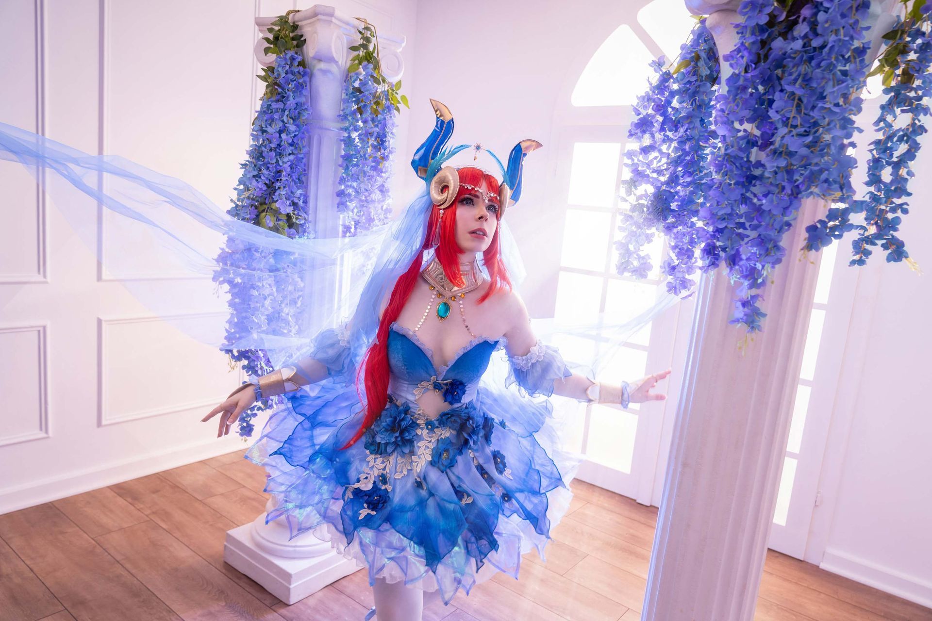 Cosplayerin in blauem Outfit posiert zwischen hängenden blauen Blumen