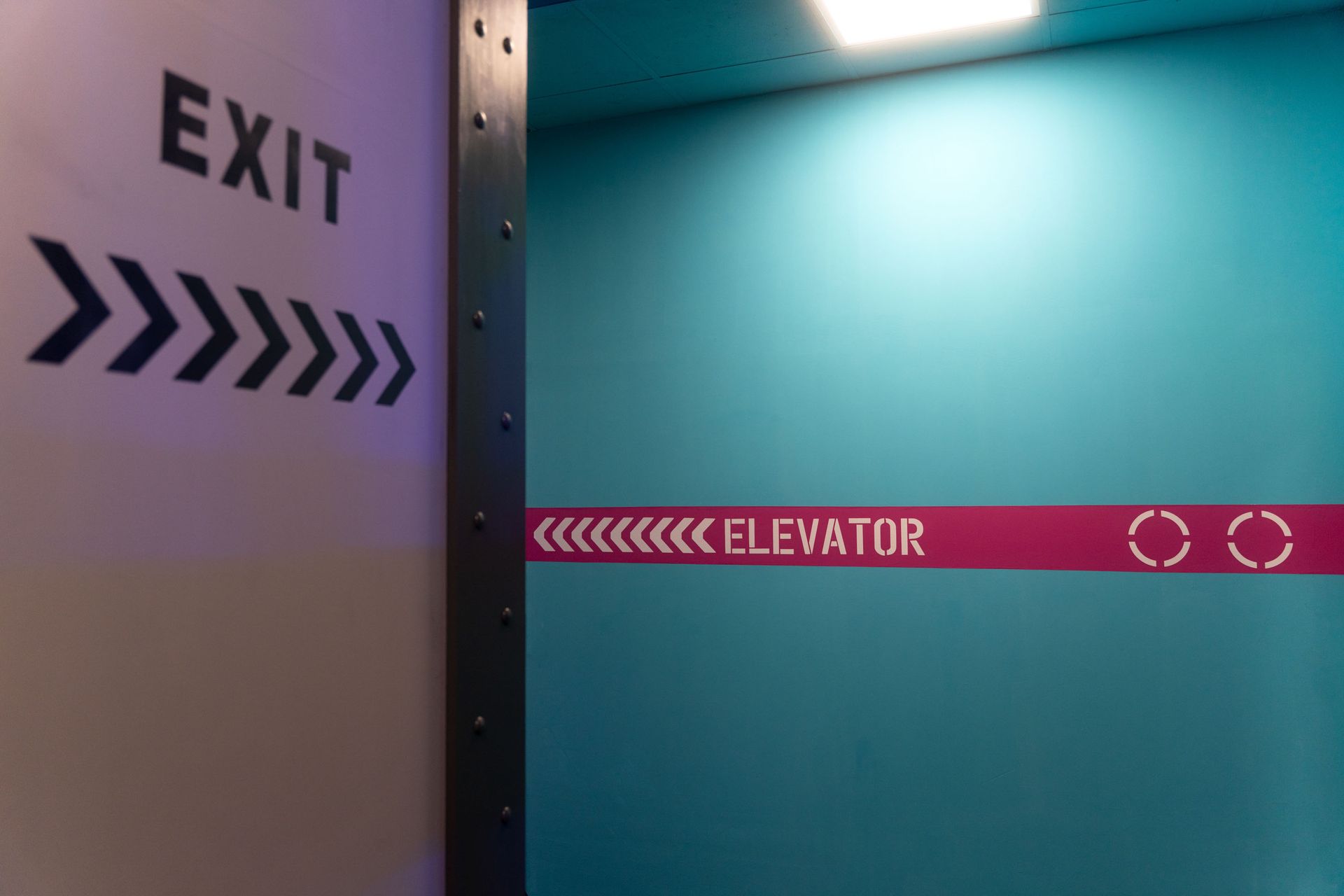 Türkise Wand mit „EXIT“-Pfeilen und rotem „ELEVATOR“-Schild