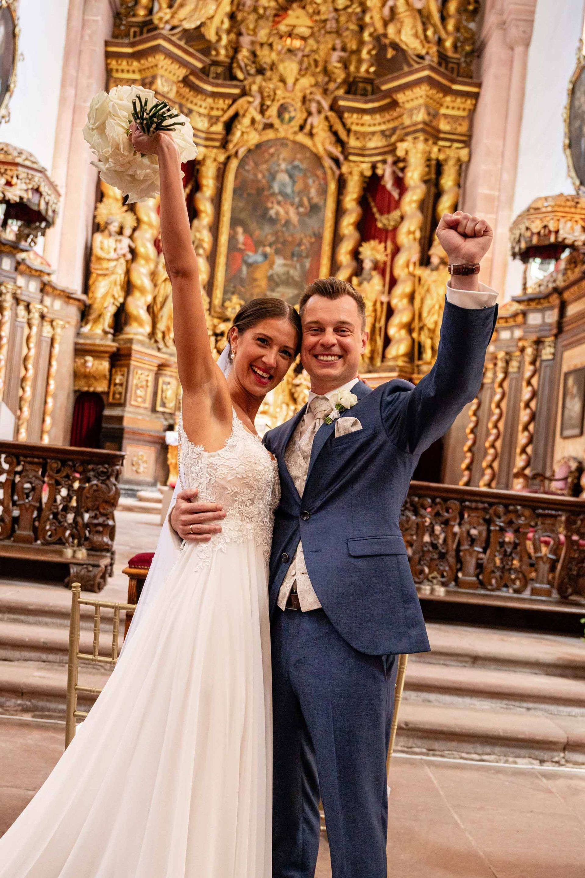 Klosterkirche im Kloster Bronnbach kirchliche Trauung, Brautpaar steht vor dem Altar. Braut und Bräutigam schauen in die Kamera und jubeln.