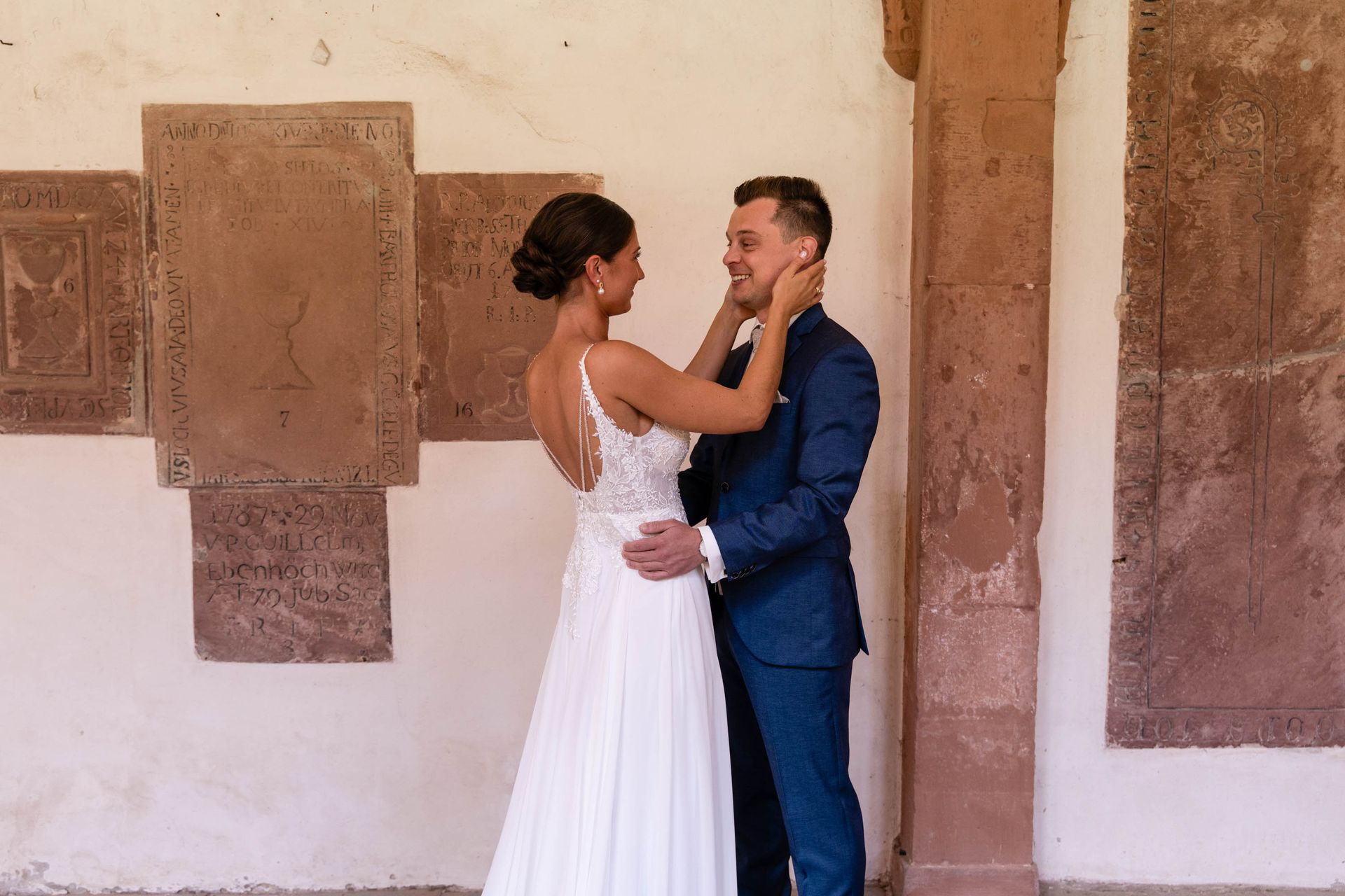 First Look im Kreuzgang Kloster Bronnbach, Braut ist beim Bräutigam und sie hlt sein Gesicht in der Hand.