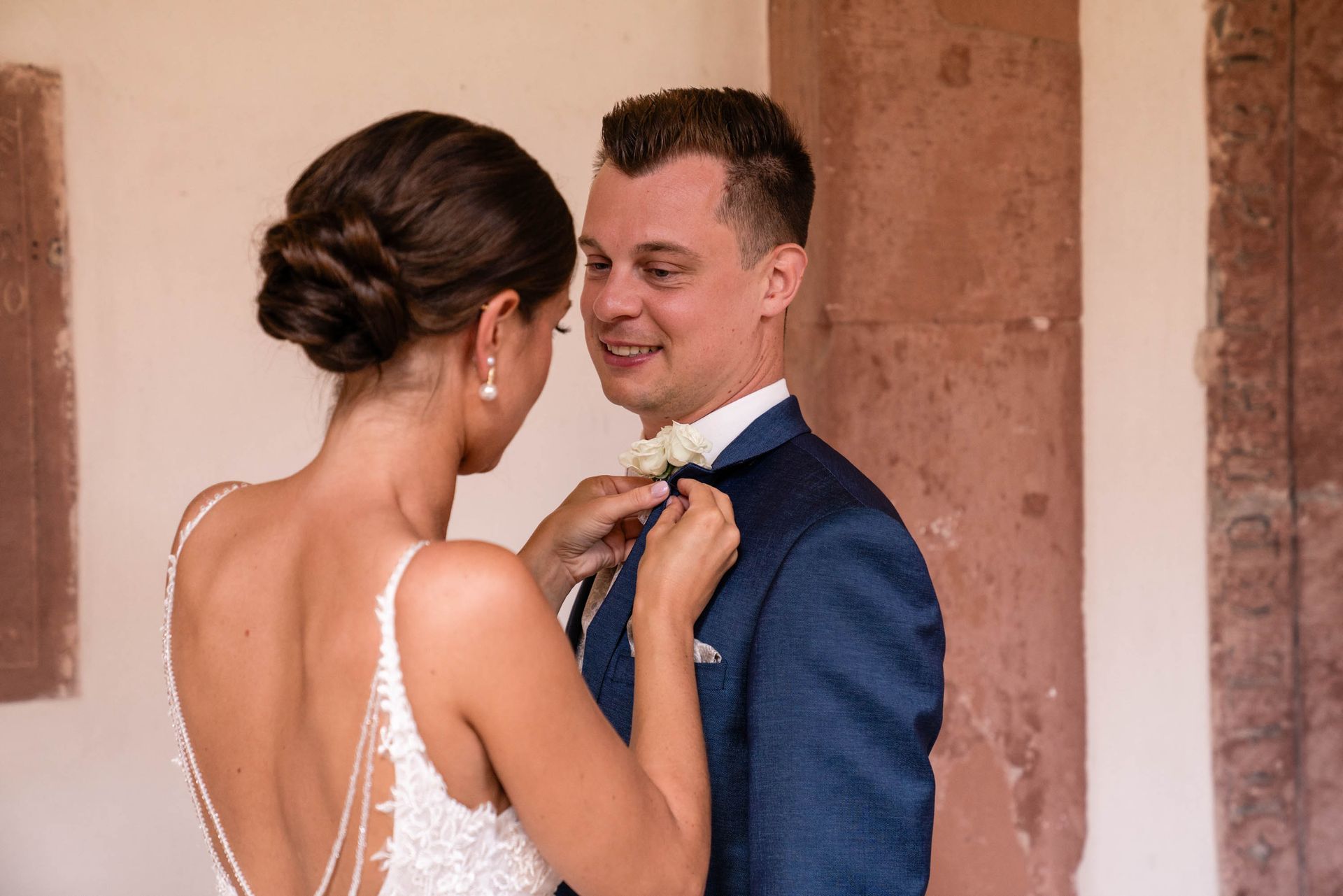 First Look im Kreuzgang Kloster Bronnbach, Braut steckt Bräutigam sein Ansteckstäußchen an.