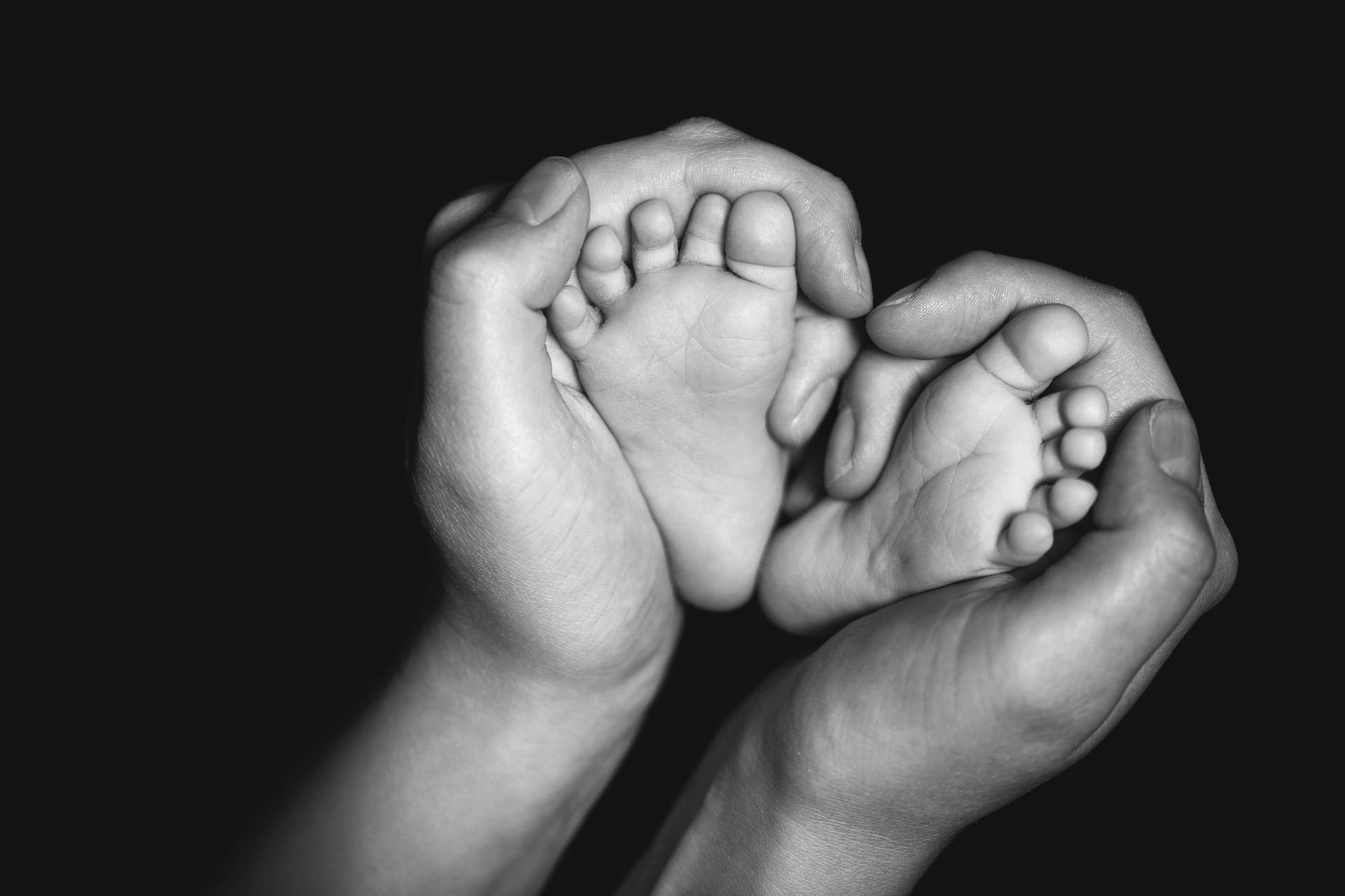 Schwarz-weiß-Nahaufnahme von erwachsenen Händen, die die Füße eines Babys halten