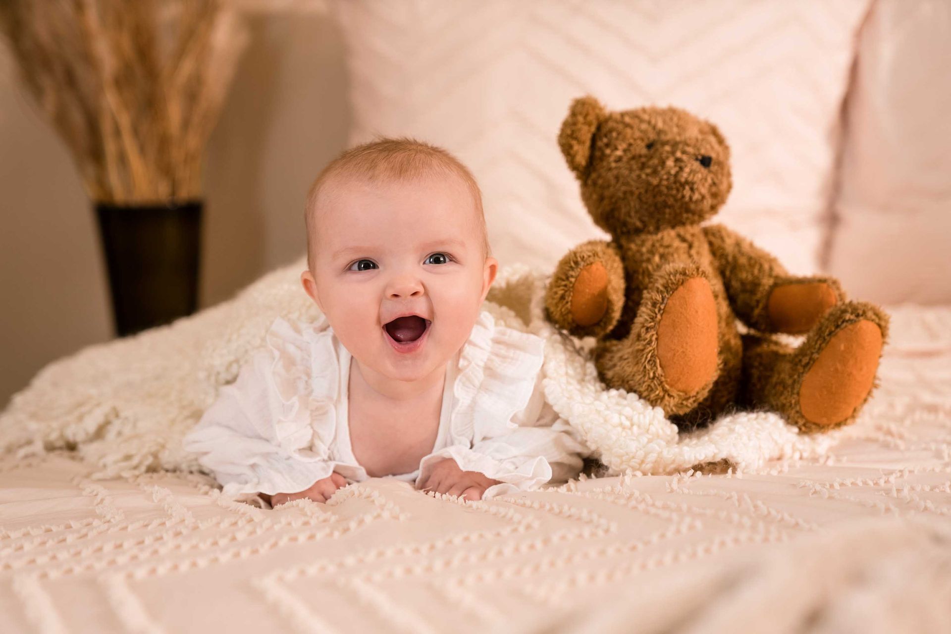 Lachendes Baby sitzt aufrecht neben einem braunen Teddybären