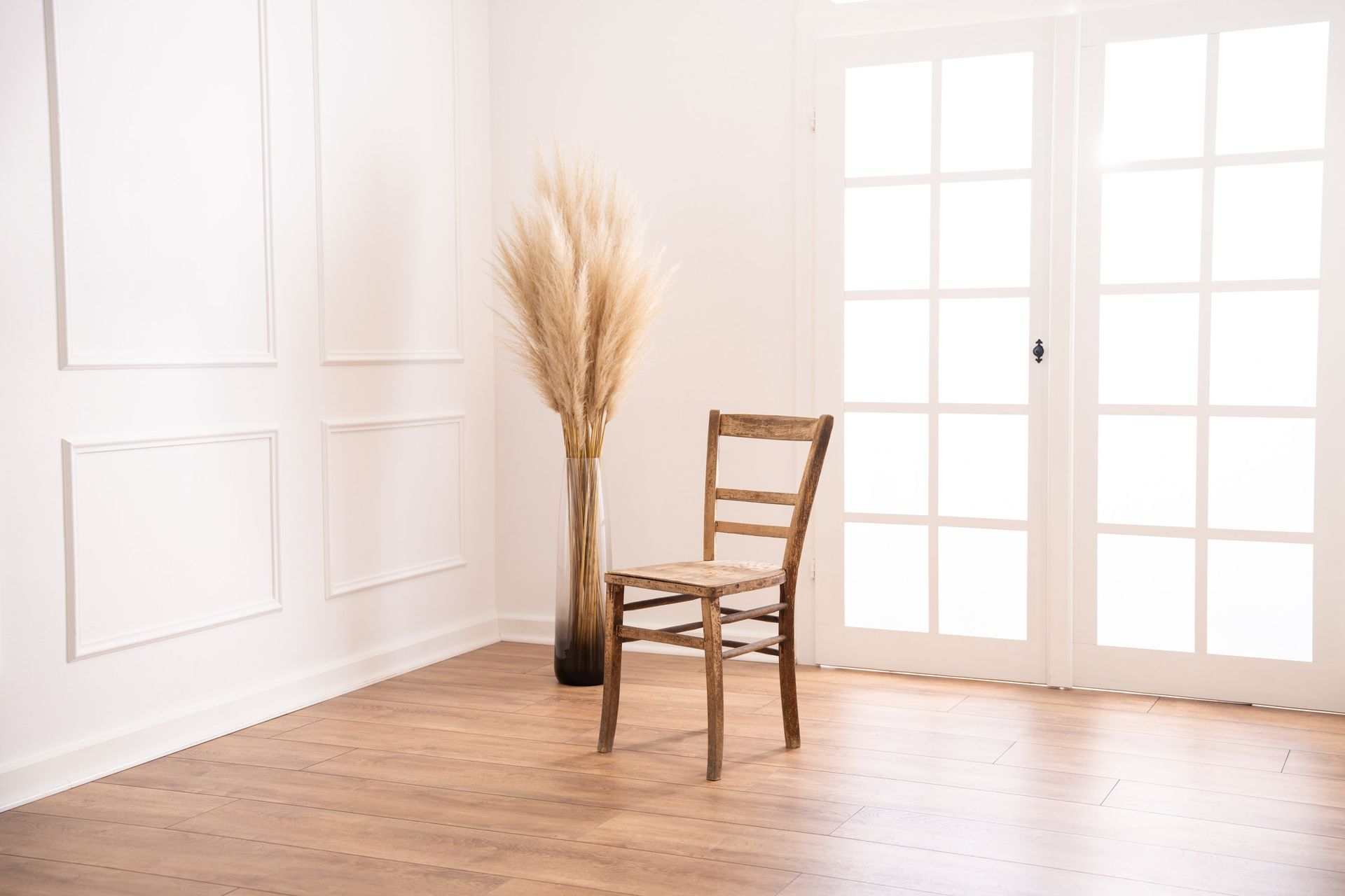 Mietstudio weißer Raum Studio zum mieten für Cosplay Fotografie. Großes weißes beleuchtetes Fenster bei weißer Barockwand mit Holzstuhl und Pampasgras.