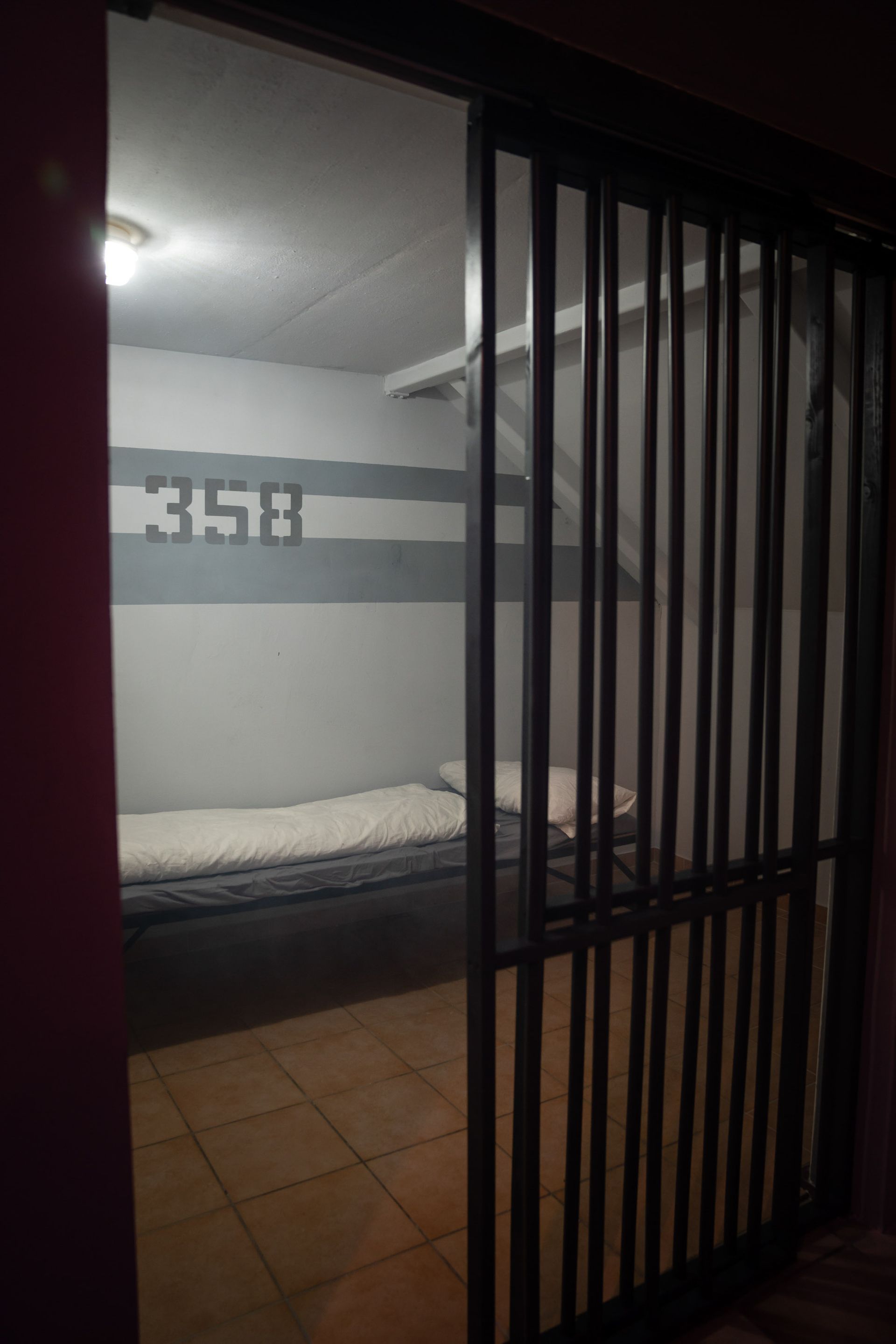 Einfache Gefängniszelle mit Bett und der Nummer 358 hinter Gittern