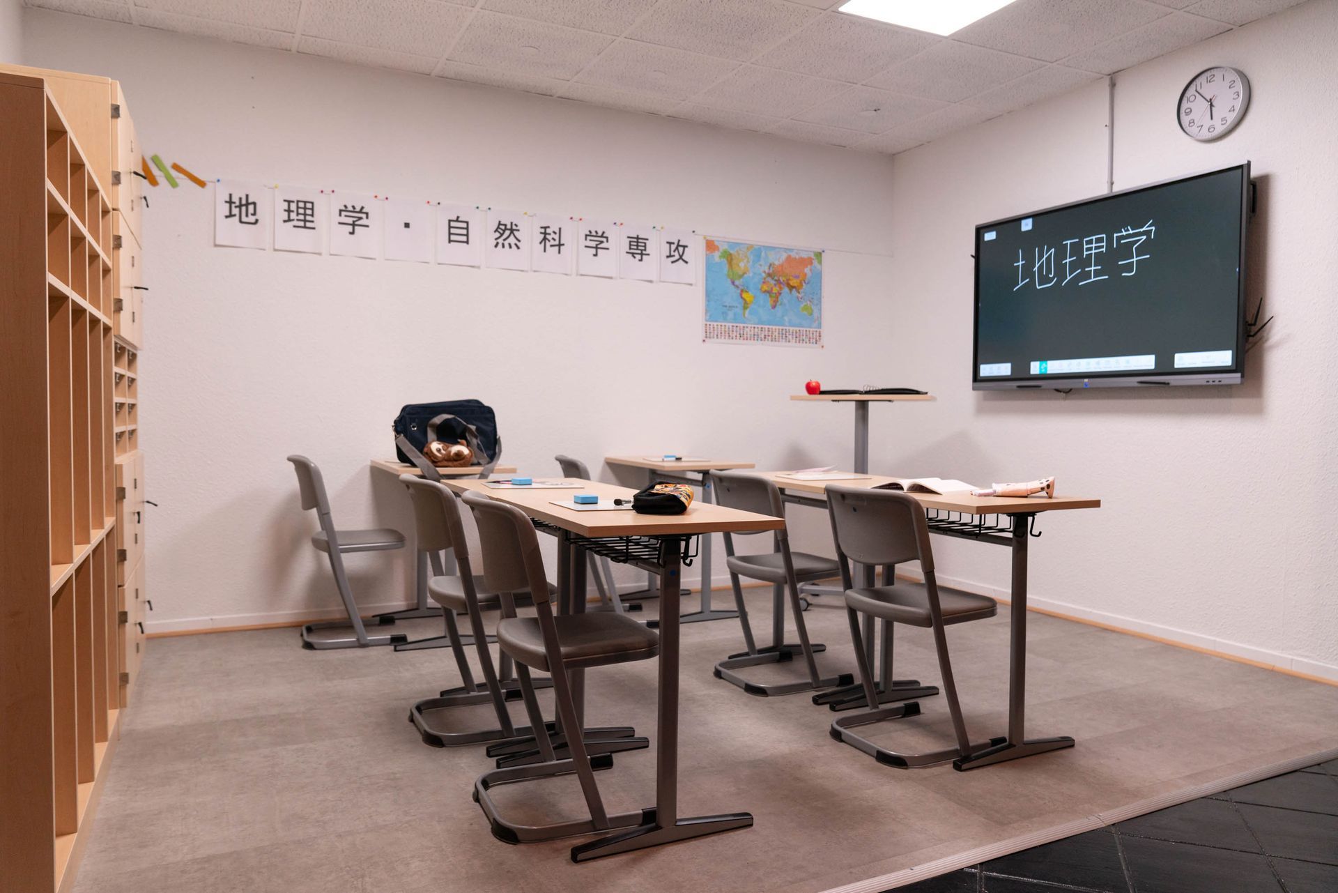 Klassenzimmer mit Tafel, Weltkarte und mehreren Schülertischen in heller, moderner Atmosphäre