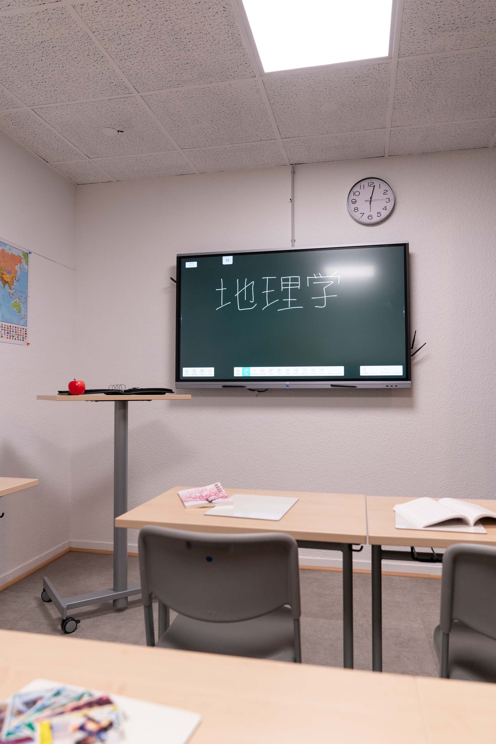 Weitwinkelaufnahme eines hellen Klassenzimmers mit mehreren Tischgruppen und Regalen im Hintergrund