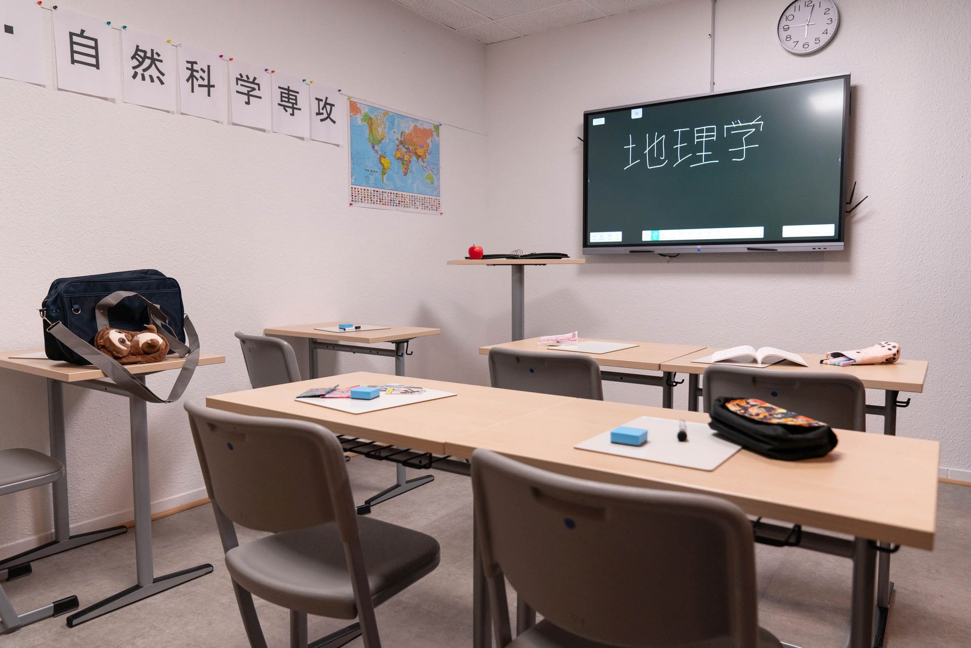 Vorderansicht eines Klassenzimmers mit Tafel, Lehrerpult und Schülertischen in geordneter Aufstellung