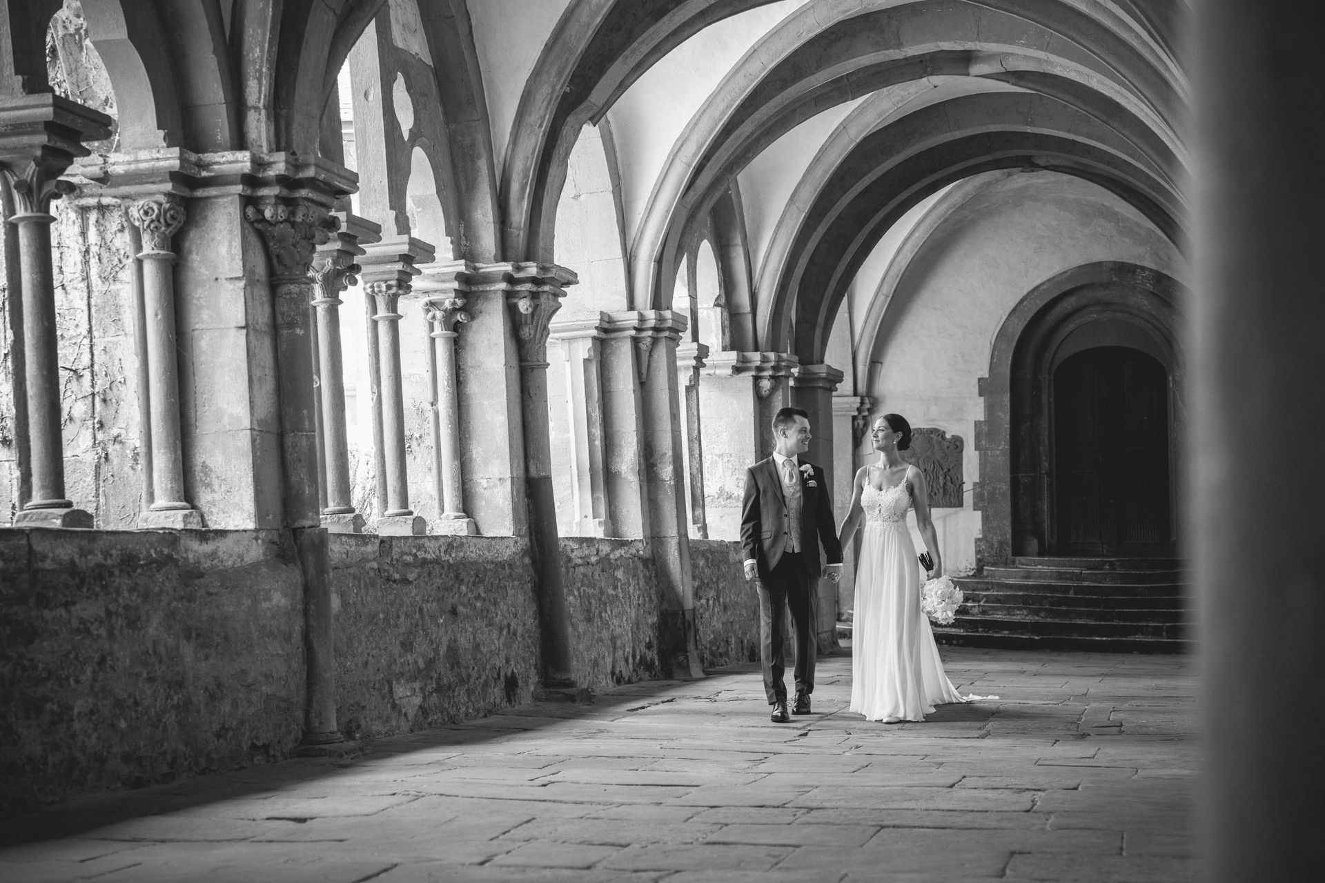 Schwarz-weiß Foto Brautpaarshooting Kloster Bronnbach im Kreuzgang. Brautpaar laufen und schauen sich an.