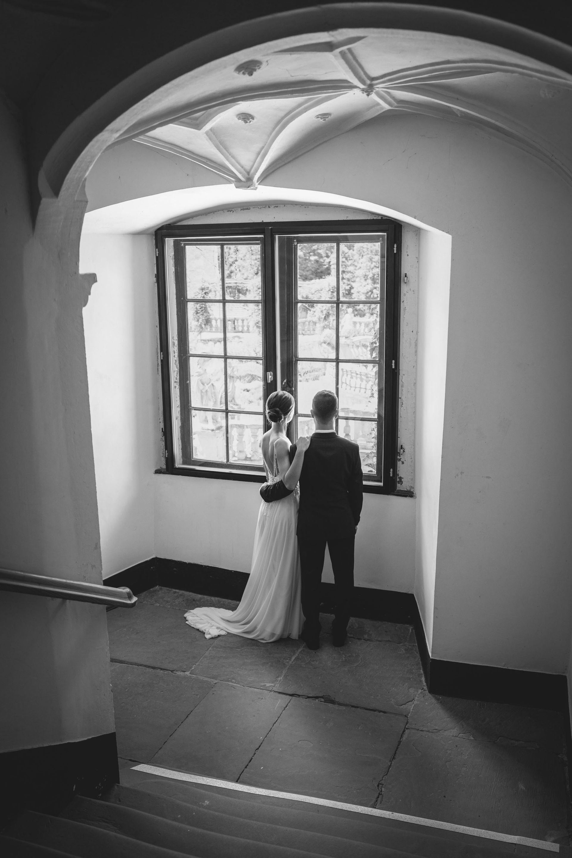 Brautpaarshooting Kloster Bronnbach im Treppenaufgang, Brautpaar schaut aus dem Fenster.