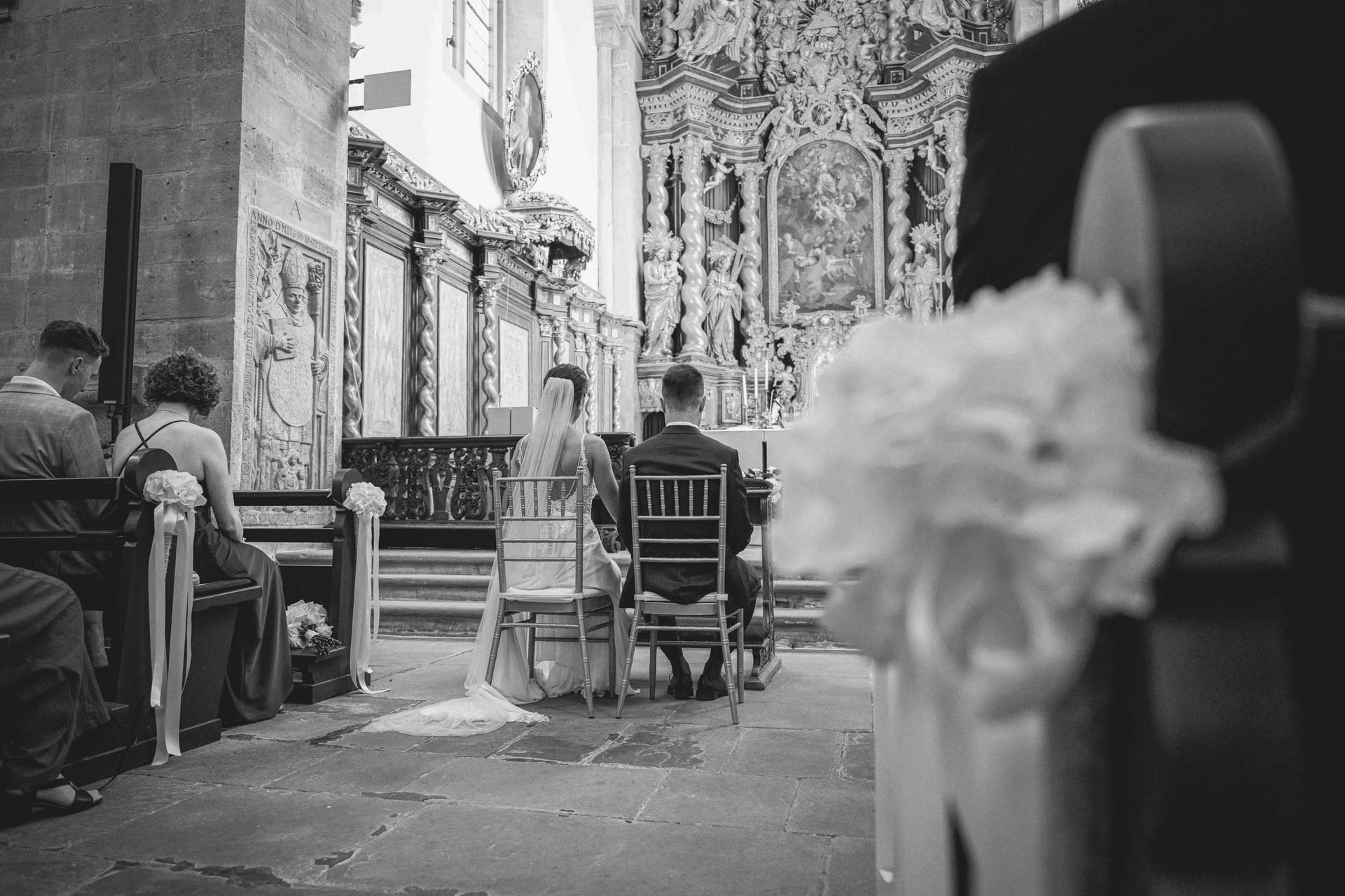 Schwarz-weiß Foto Klosterkirche im Kloster Bronnbach kirchliche Trauung, Brautpaar sitz vor dem Altar. Blume im Vordergrund.