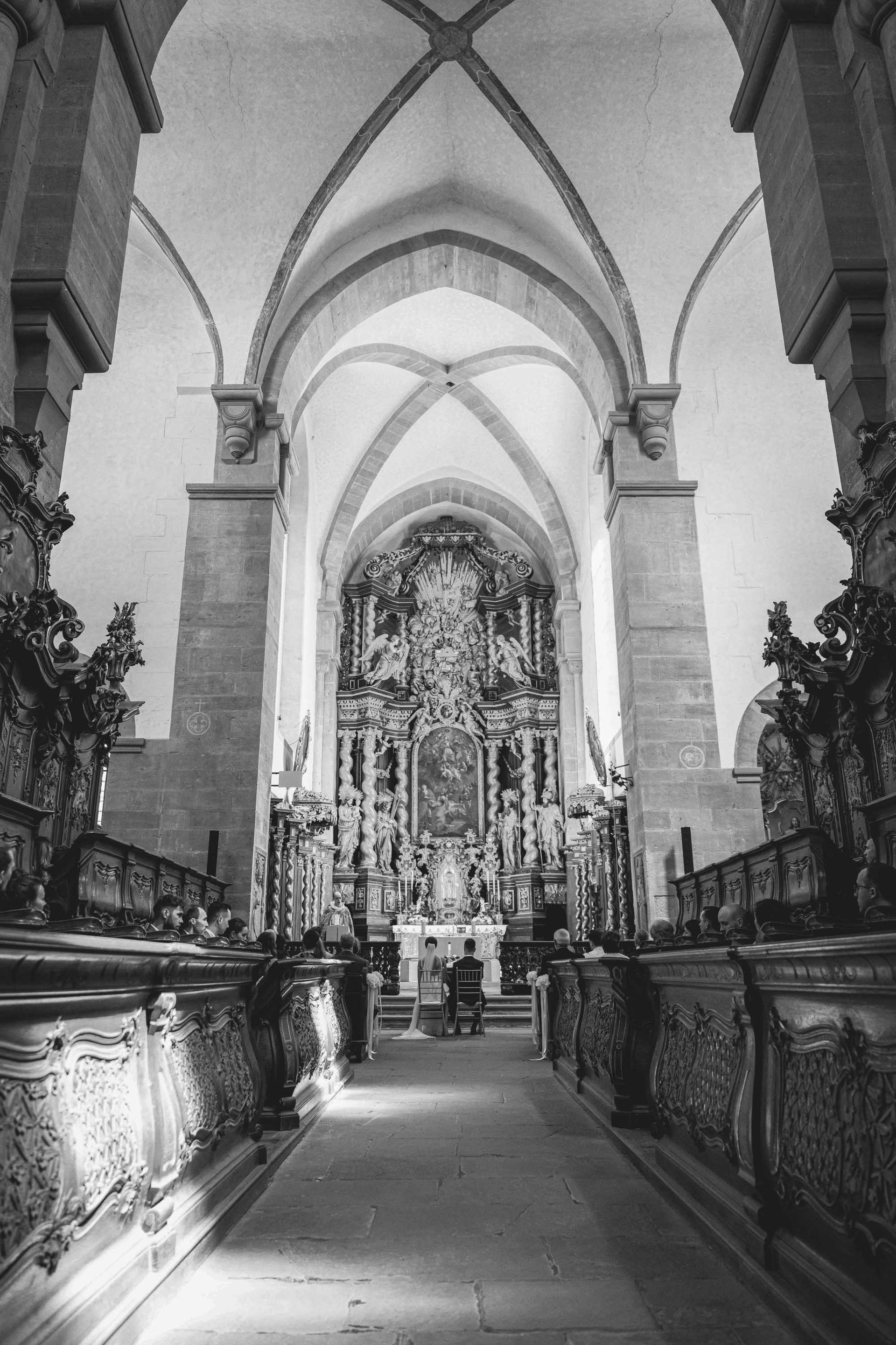 Schwarz-weiß Foto Klosterkirche im Kloster Bronnbach kirchliche Trauung, Brautpaar sitz vor dem Altar. Aufnahme von der Ferne.