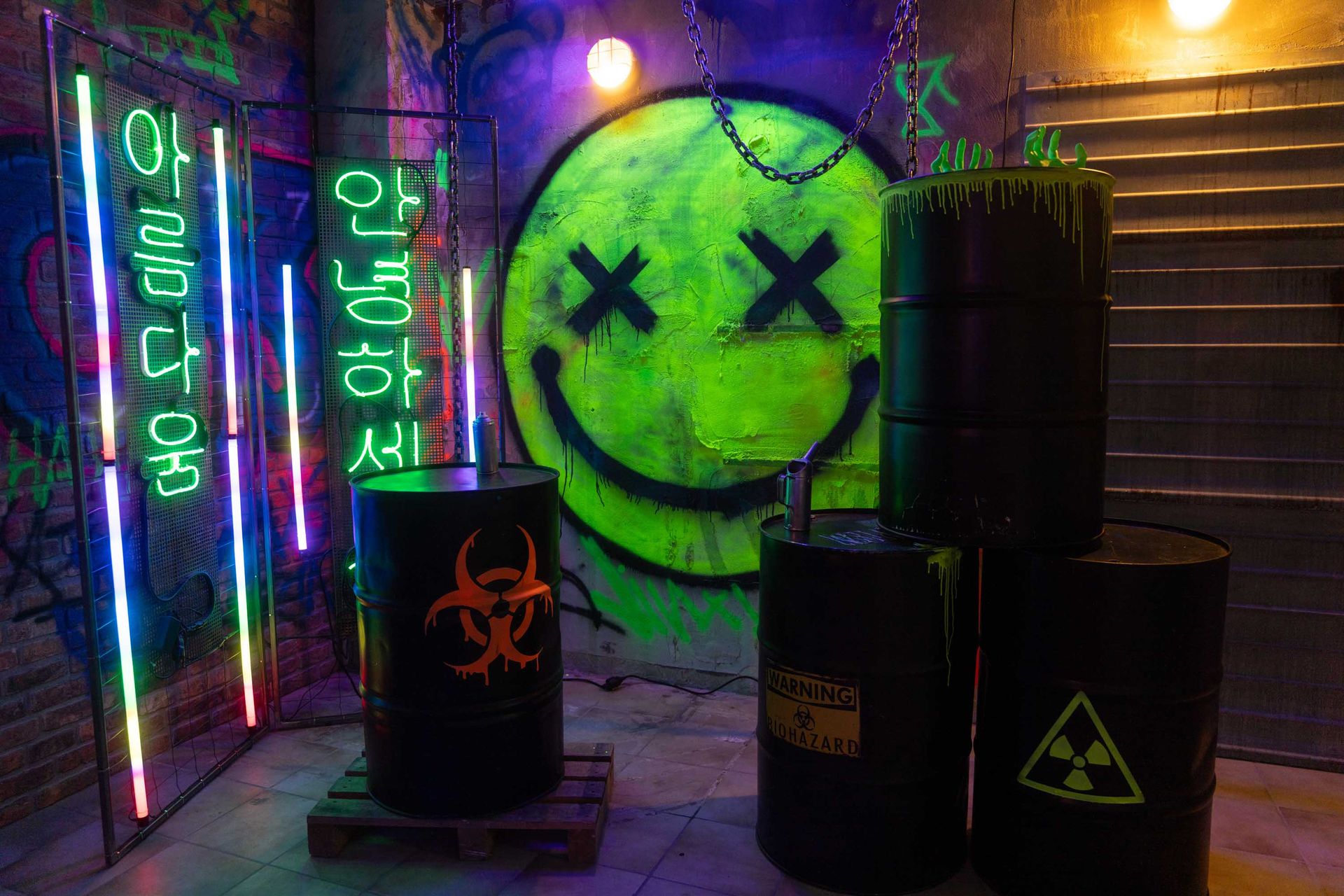 Futuristisches Lost-Place-Set mit großem grünem Smiley, Neon-Schildern und stapelbaren Gefahrgut-Fässern