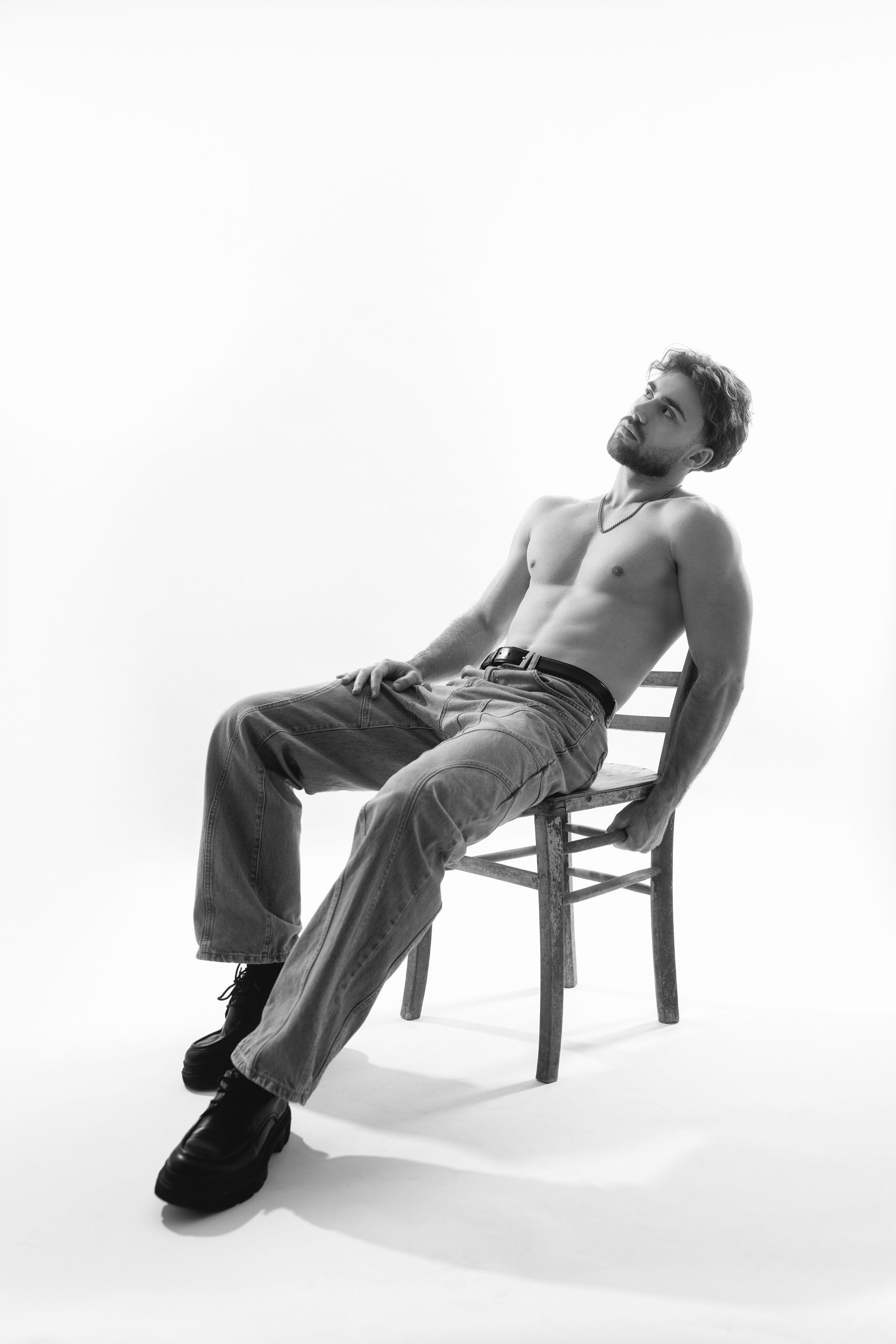 Seitliches Portrait eines Mannes mit Bart und Kette, shirtless vor weißem Hintergrund