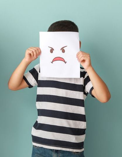 Child holding a drawing of a grumpy face over their own face.