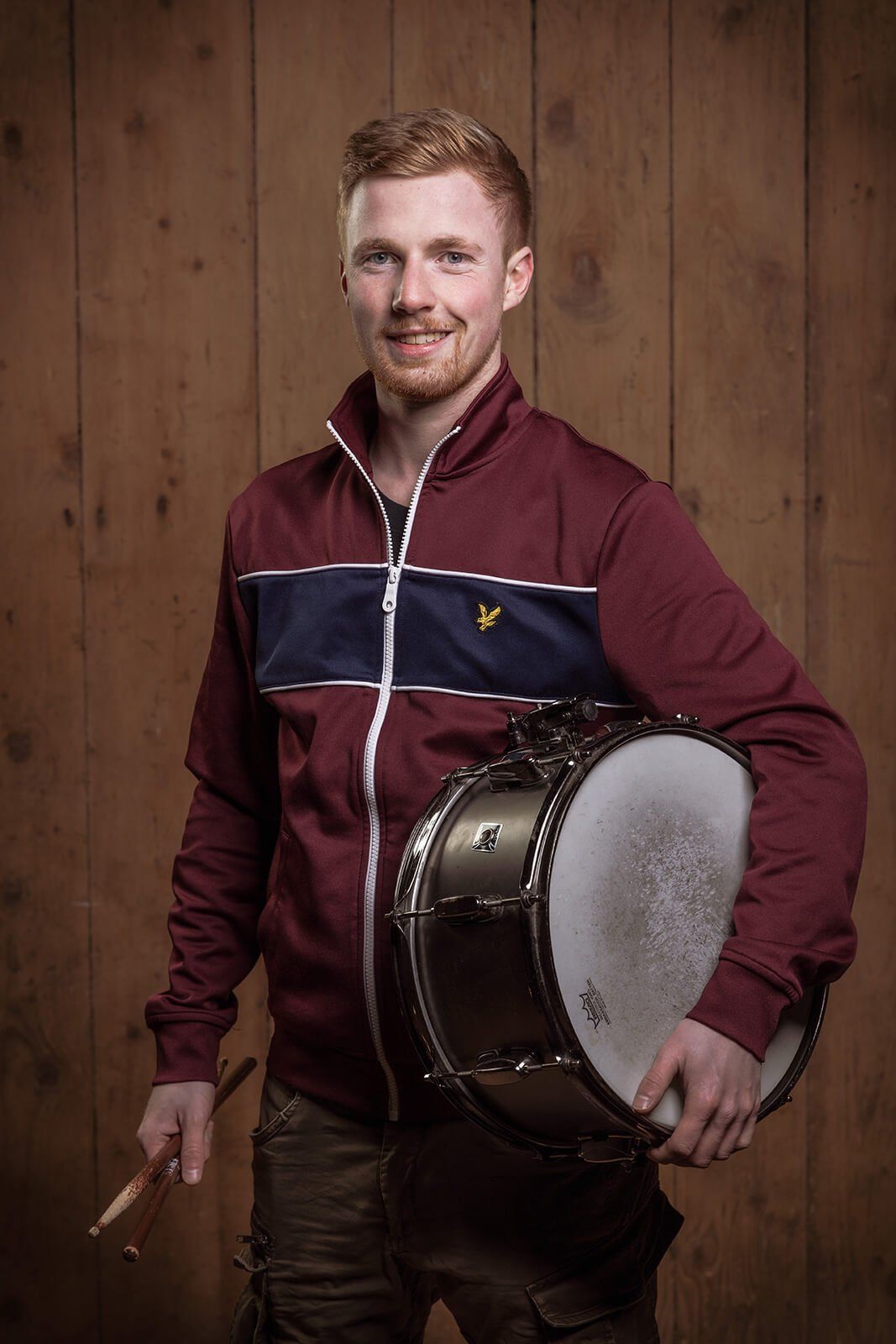 Portrait ab Hüfte von Schlagzeuger Christoph mit Trommel vor Holzwand
