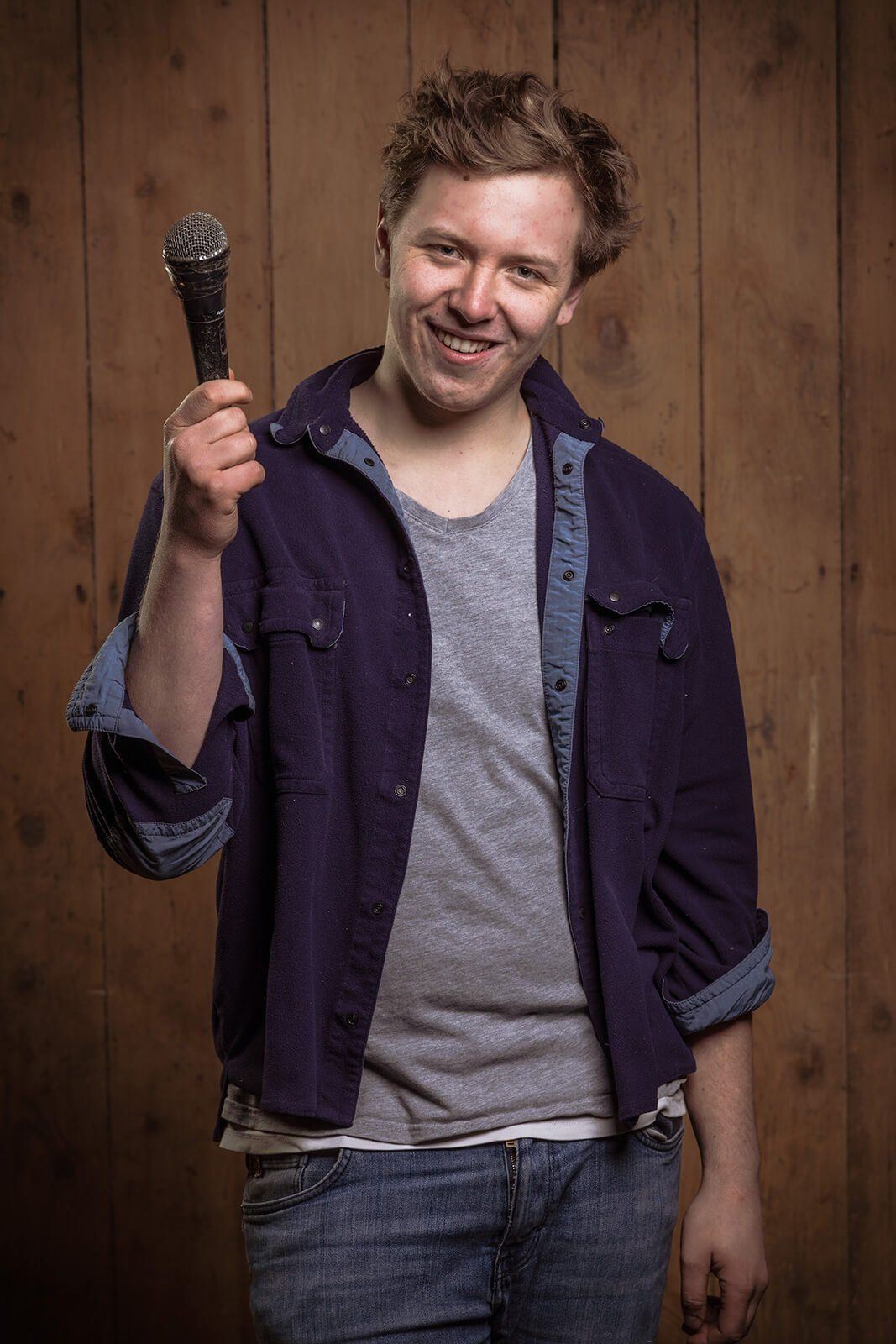 Portrait ab Hüfte von Frontsänger Christian mit Mikrofon vor Holzwand