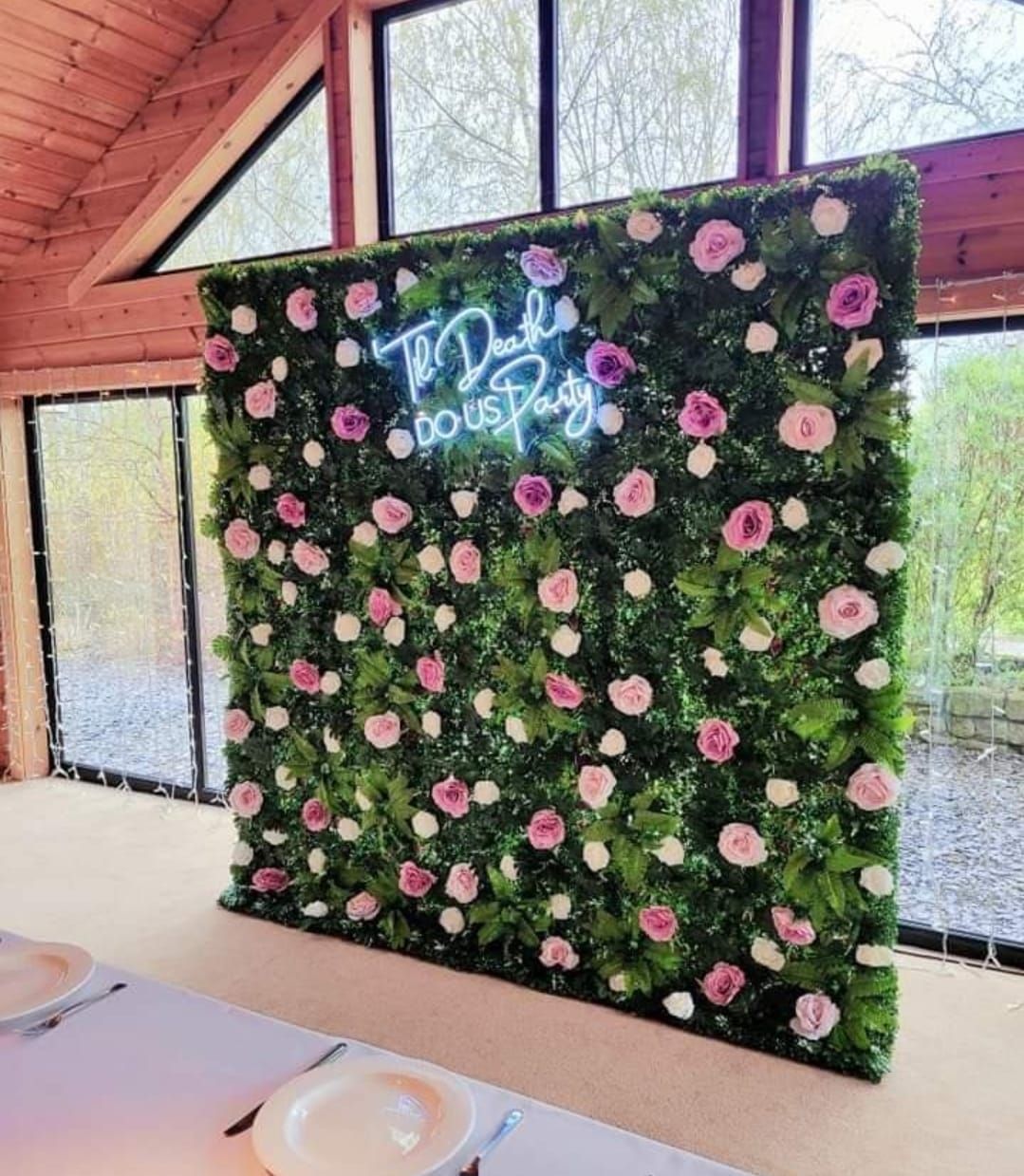 Til death do us party neon sign on green foliage flower wall creating a backdrop.