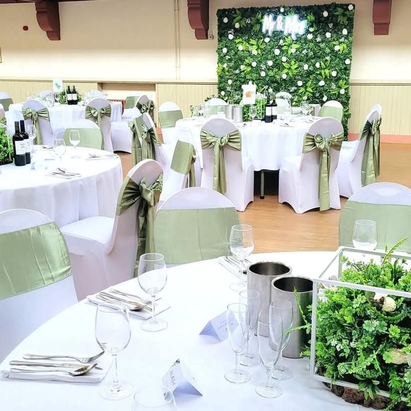 Sage green wedding reception setup with green foliage wall and neon sign fitted.