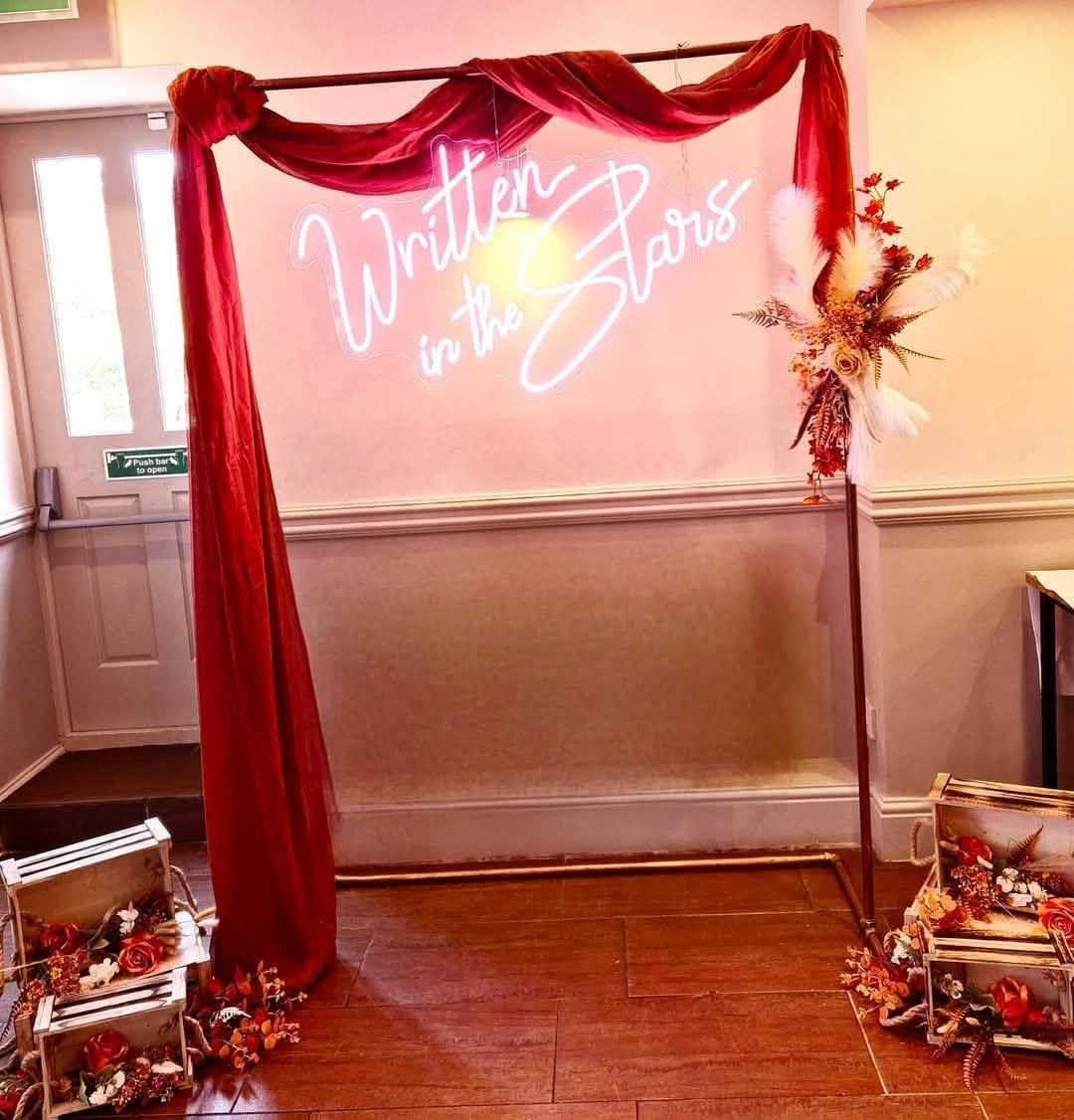 Written in the stars neon sign on copper frame with burnt orange foliage and draping.