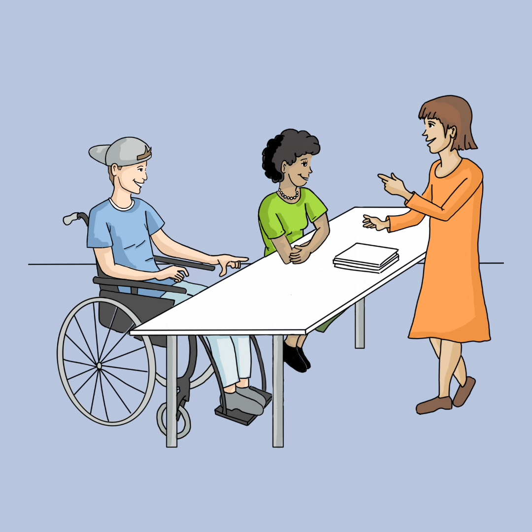 Ein Junge im Rollstuhl, eine Frau mit grüner Bluse und eine weitere Frau in einem orangefarbenen Kleid stehen bzw. sitzen an einem Tisch mit Papieren und sprechen miteinander.