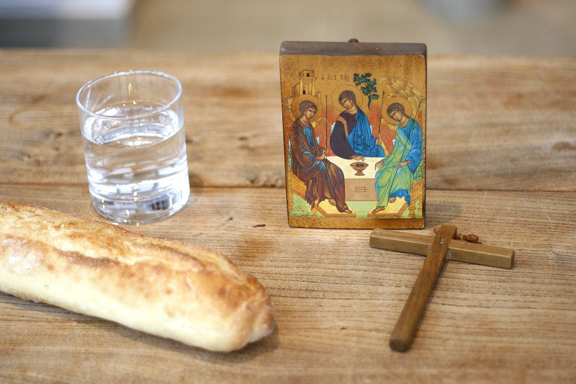 Tischplatte mit Brot, einem Glas Wasser, einem Kreuz und einem Bild von Jesus mit zwei Jüngern